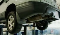 Underside of a gray SUV on a lift in an auto repair shop, with the rear wheel visible
