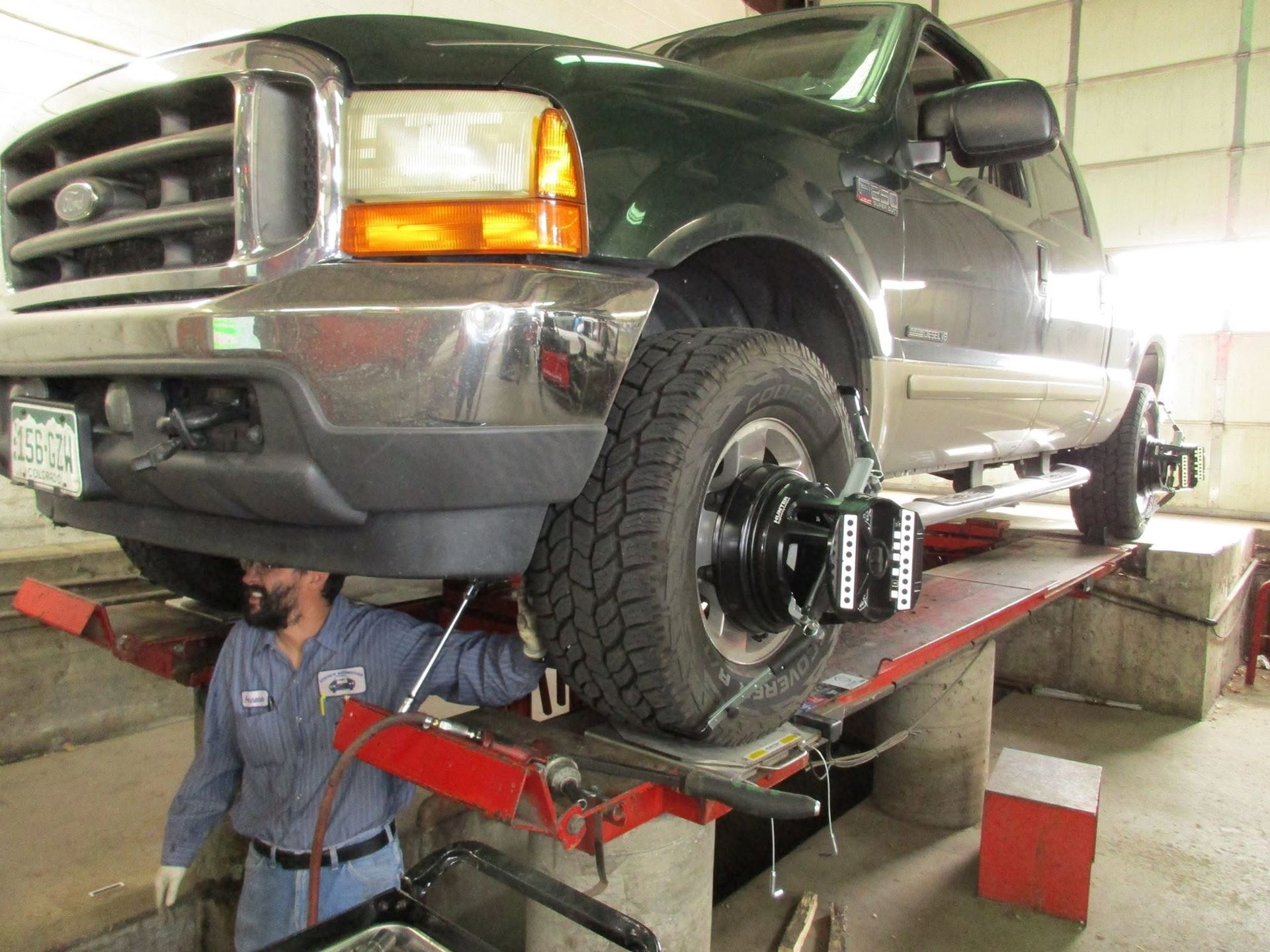 Green pickup truck on a lift in an auto shop, with a mechanic working underneath