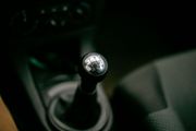 Close-up of a manual car gear shift knob in a dark interior with cup holders nearby