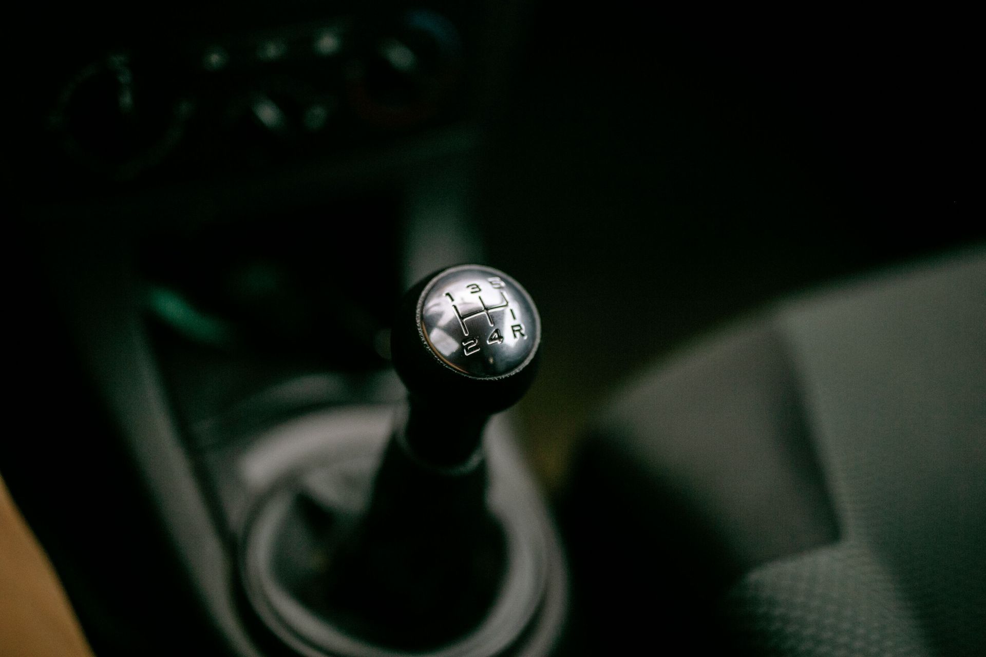 Close-up of a manual car gear shift knob in a dark interior with cup holders nearby