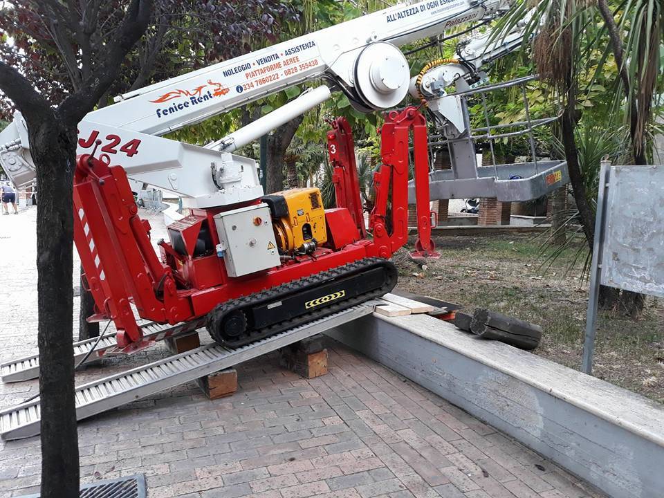 Elevatore cingolato rosso e bianco su una rampa, vicino agli alberi. Macchinari industriali.
