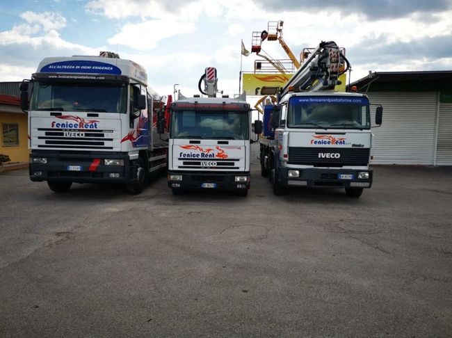 Tre camion bianchi con piattaforme aeree parcheggiati all'esterno.