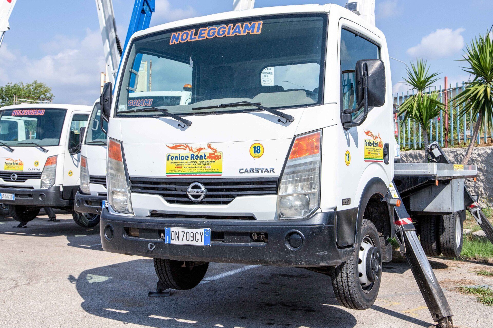 Camion Nissan Cabstar bianco con gru, parcheggiato all'esterno. Scritta 