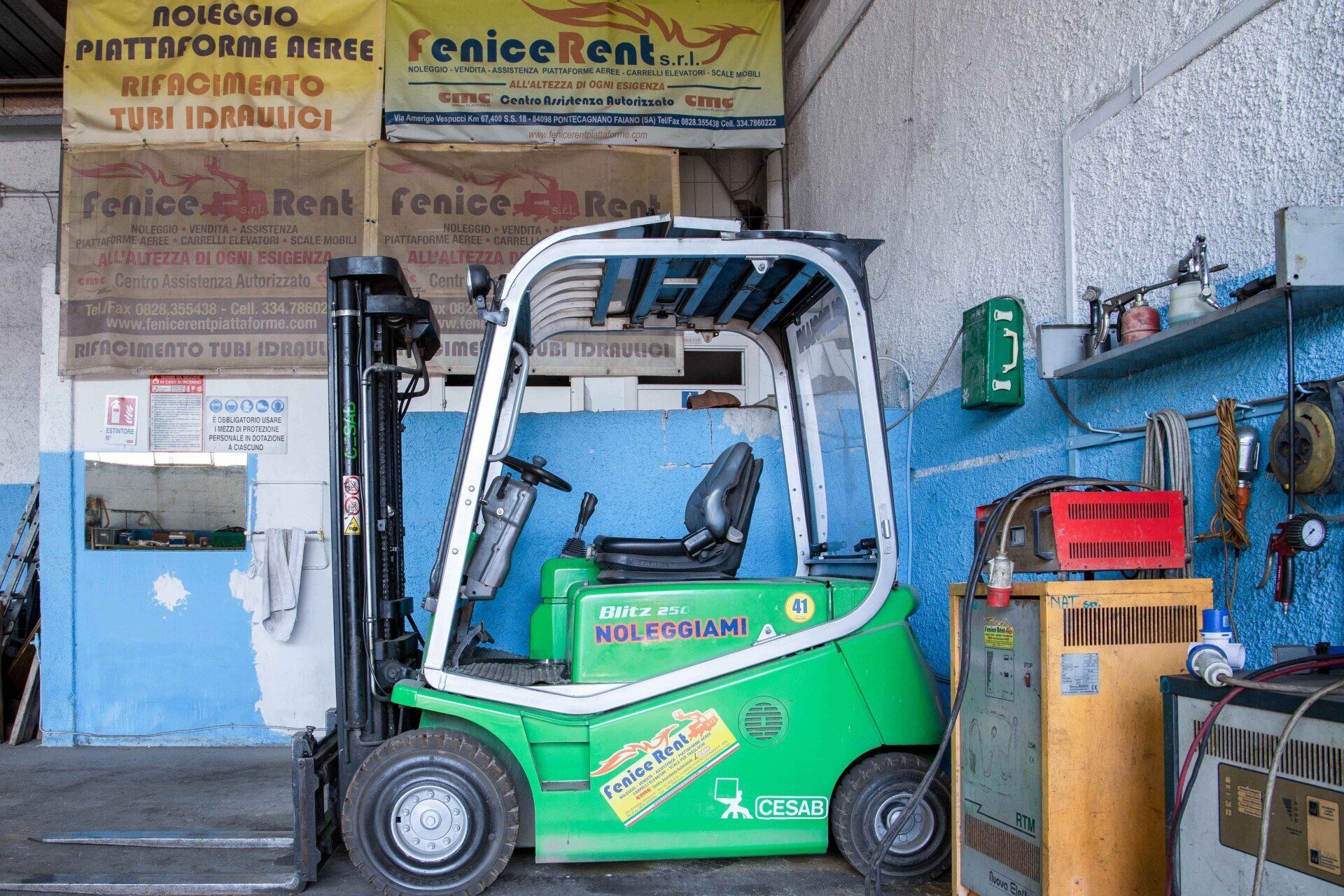 Carrello elevatore verde in un garage con attrezzi e cartelli.