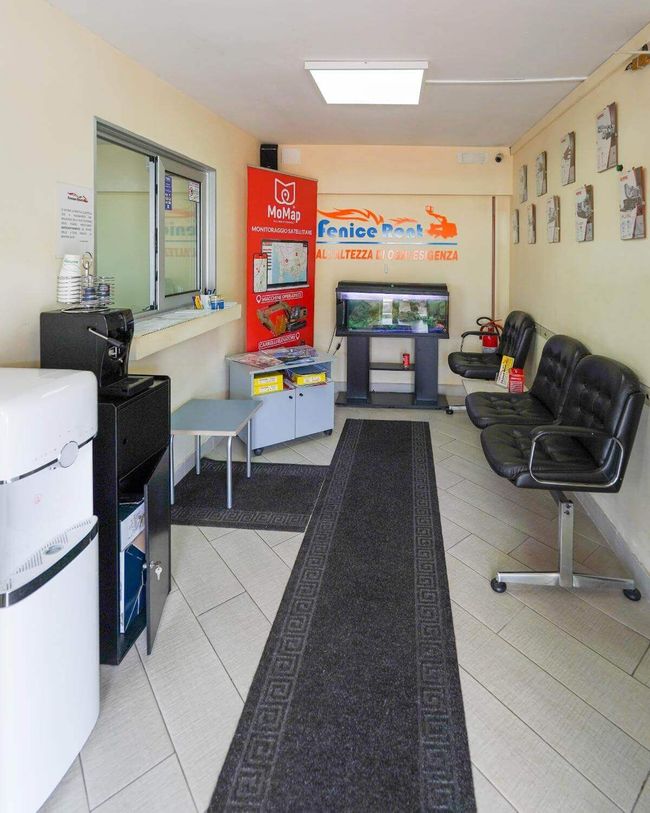Sala d'attesa di un'attività commerciale con sedie nere, acquario e bancone per il servizio.