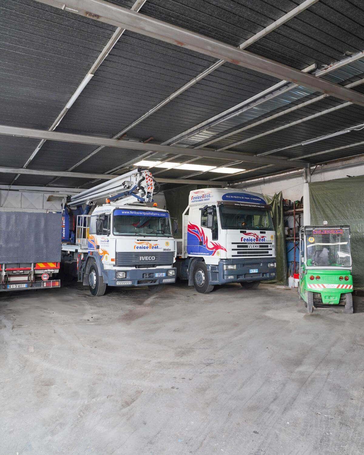 Camion e un carrello elevatore all'interno di un magazzino. Camion bianchi con dettagli blu. Pavimento in cemento grigio.