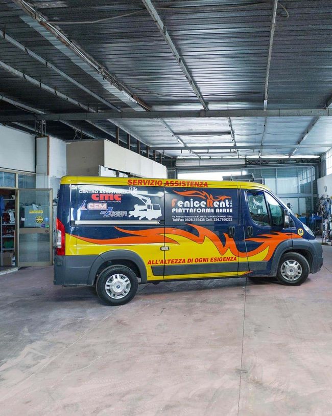 Furgone blu e giallo con grafica parcheggiato in un garage. Testo: 