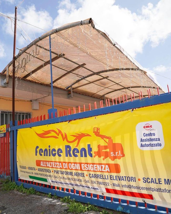 Striscione giallo per Fenice Rent srl davanti a un edificio con tenda da sole beige e recinzione blu.