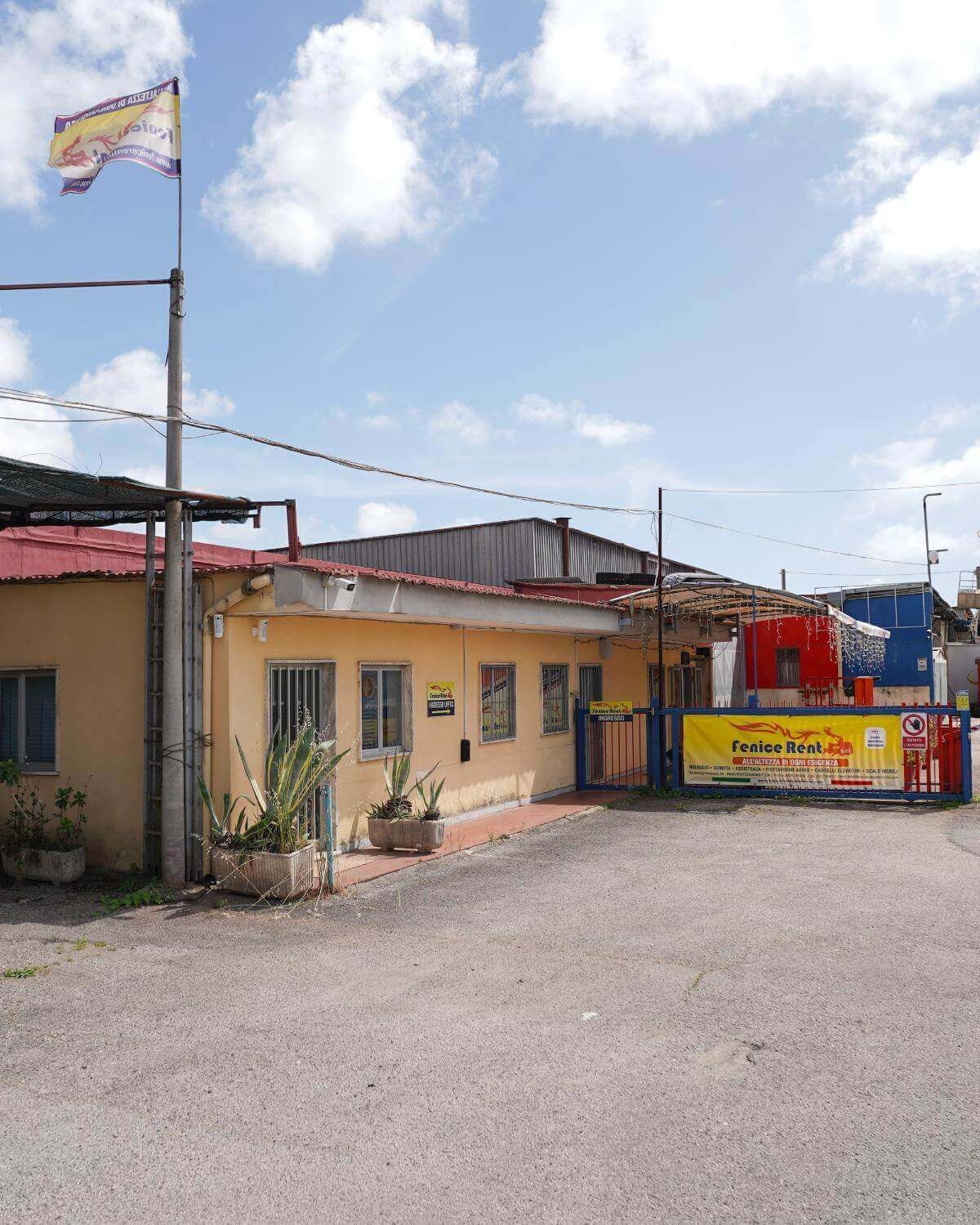 Edificio giallo con tetto, bandiera e cancello rossi, con uno striscione che recita 