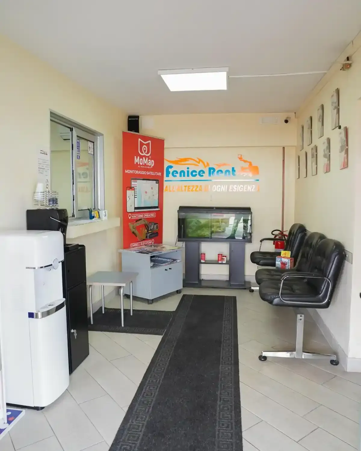 Sala d'attesa con sedie nere, acquario e un refrigeratore d'acqua. Cartello con la scritta 