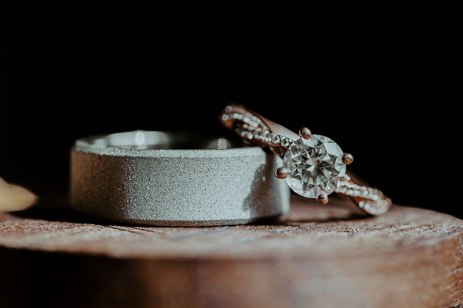 Wedding rings, a diamond engagement ring and a textured wedding band, resting on wood.