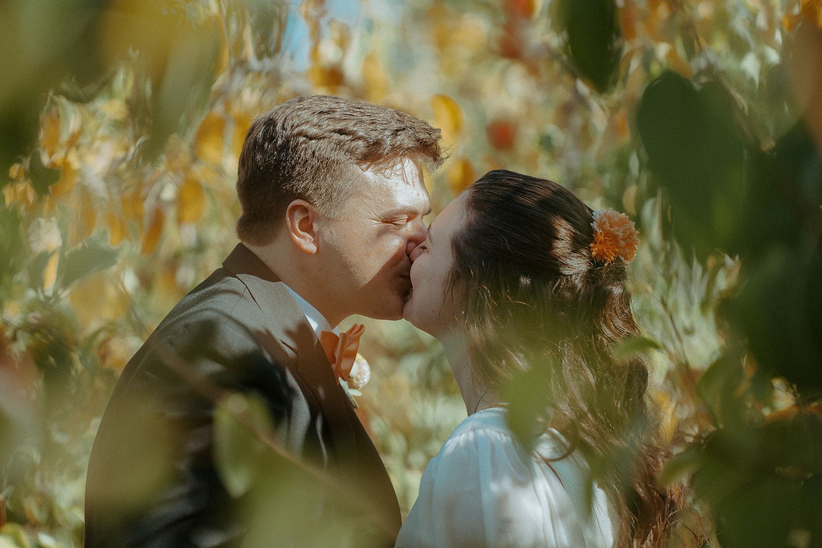 A bride and groom are kissing in a field of trees.
