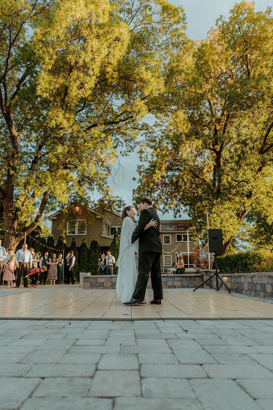 A bride and groom are dancing on a dance floor in front of trees.