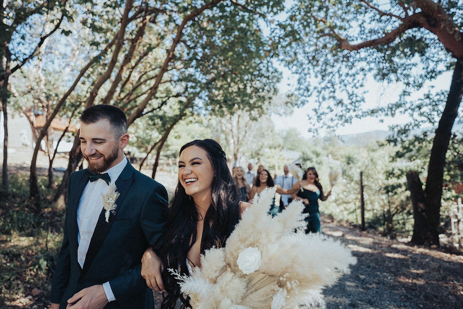 A bride and groom are walking down a path with their wedding party.