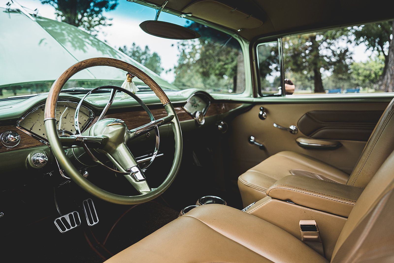 The interior of an old car with brown leather seats and a wooden steering wheel.