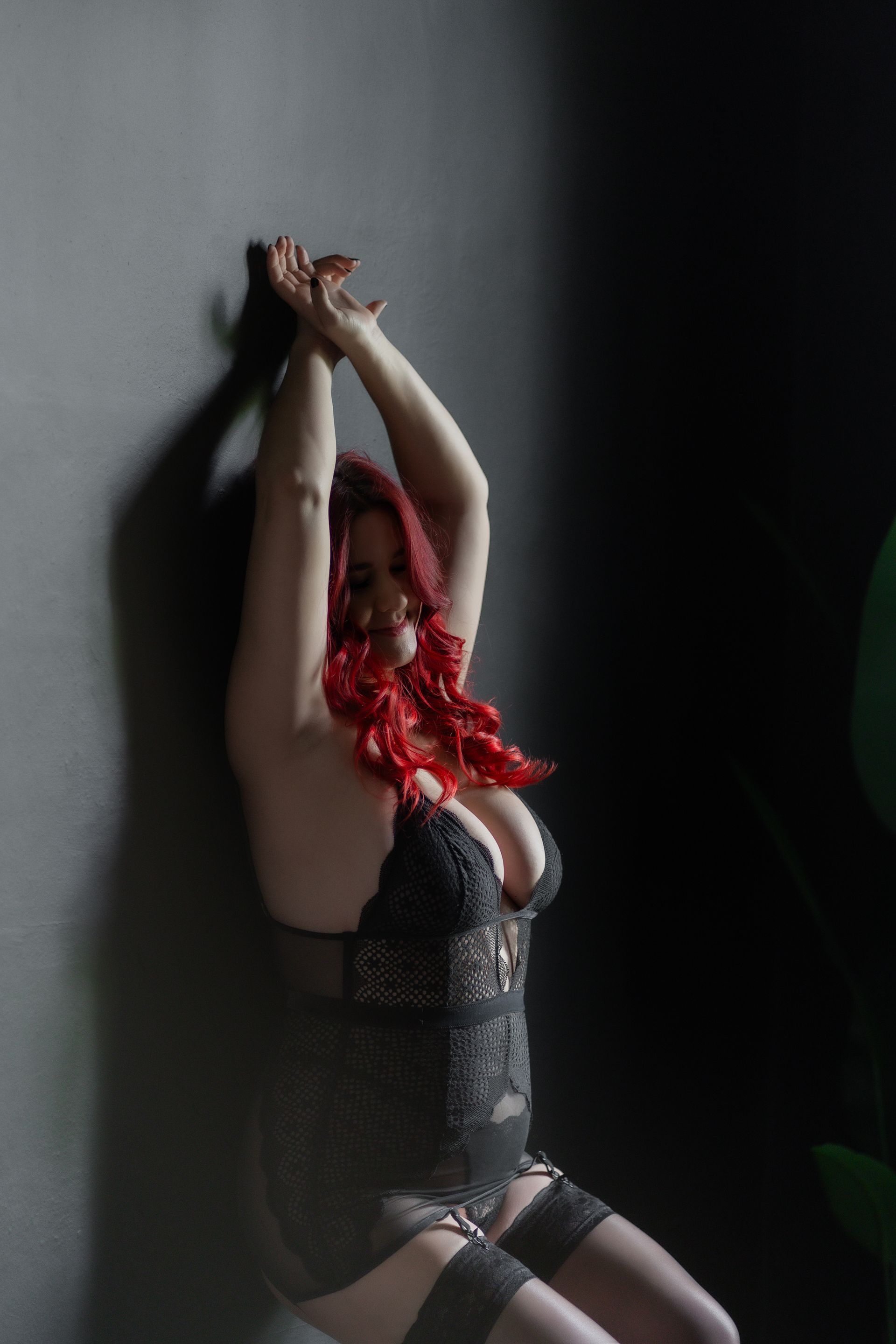 A woman with red hair is sitting in front of a wall with her arms up.