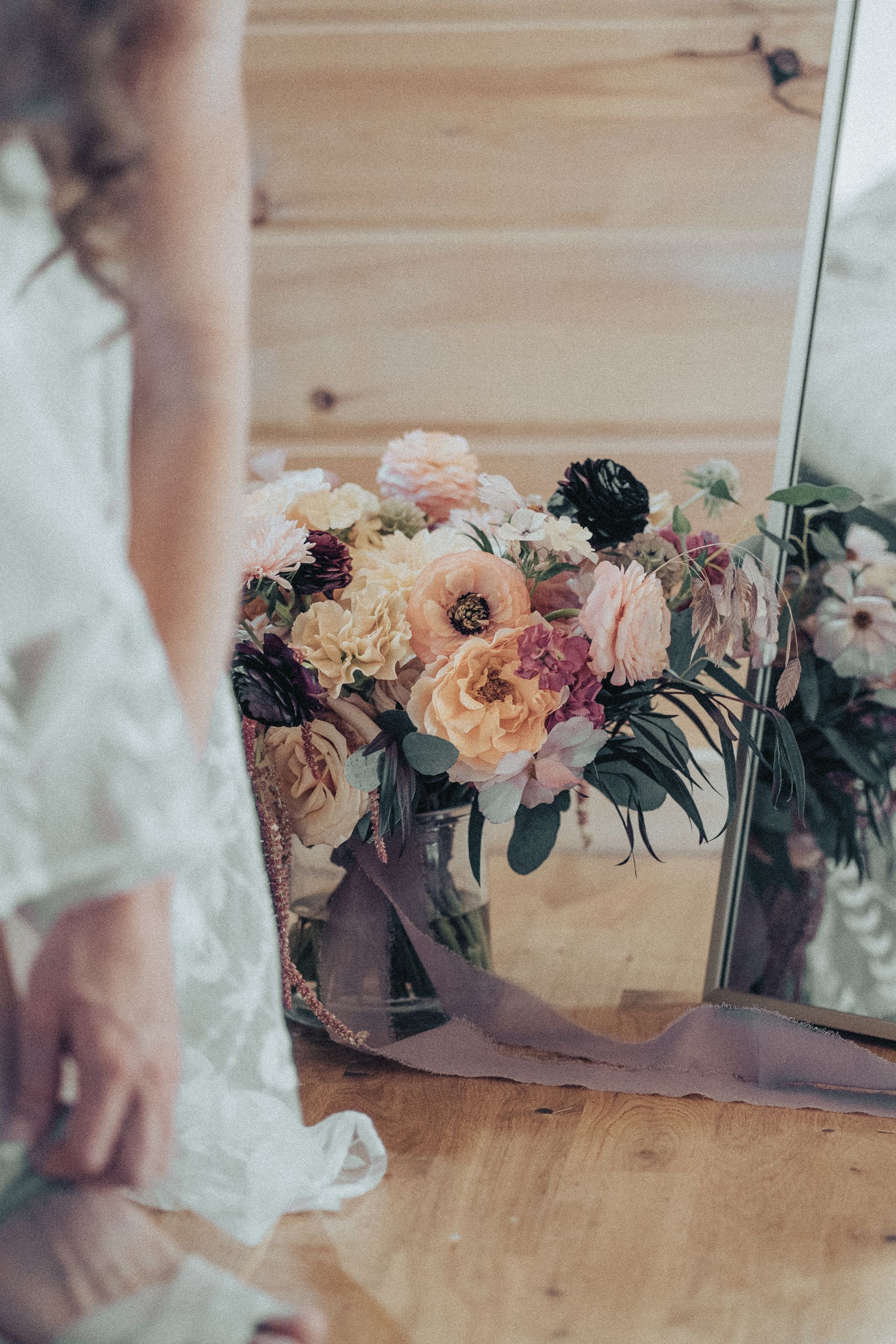 A woman is looking at her reflection in a mirror while holding a bouquet of flowers.