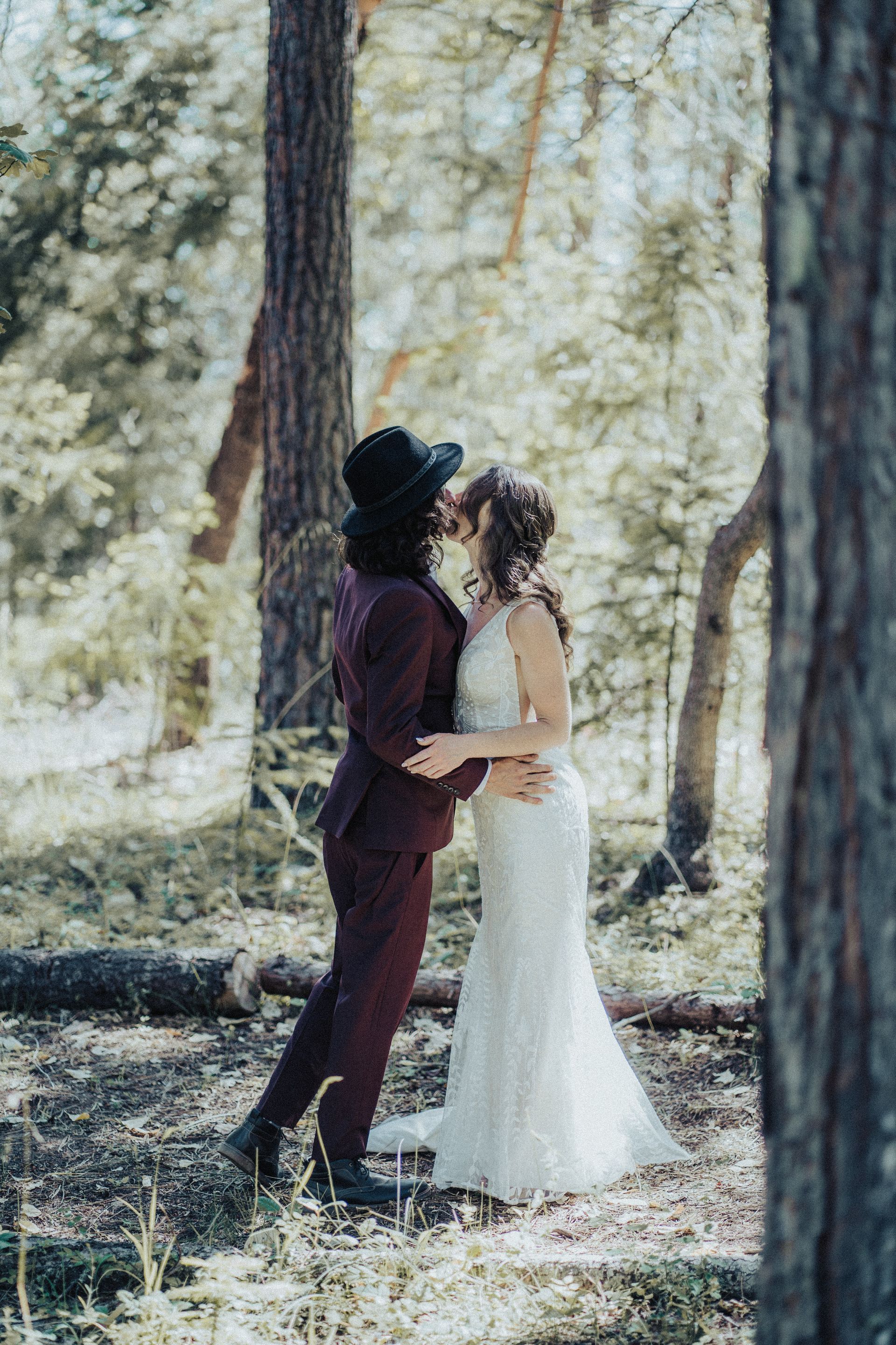 A bride and groom are kissing in the woods.