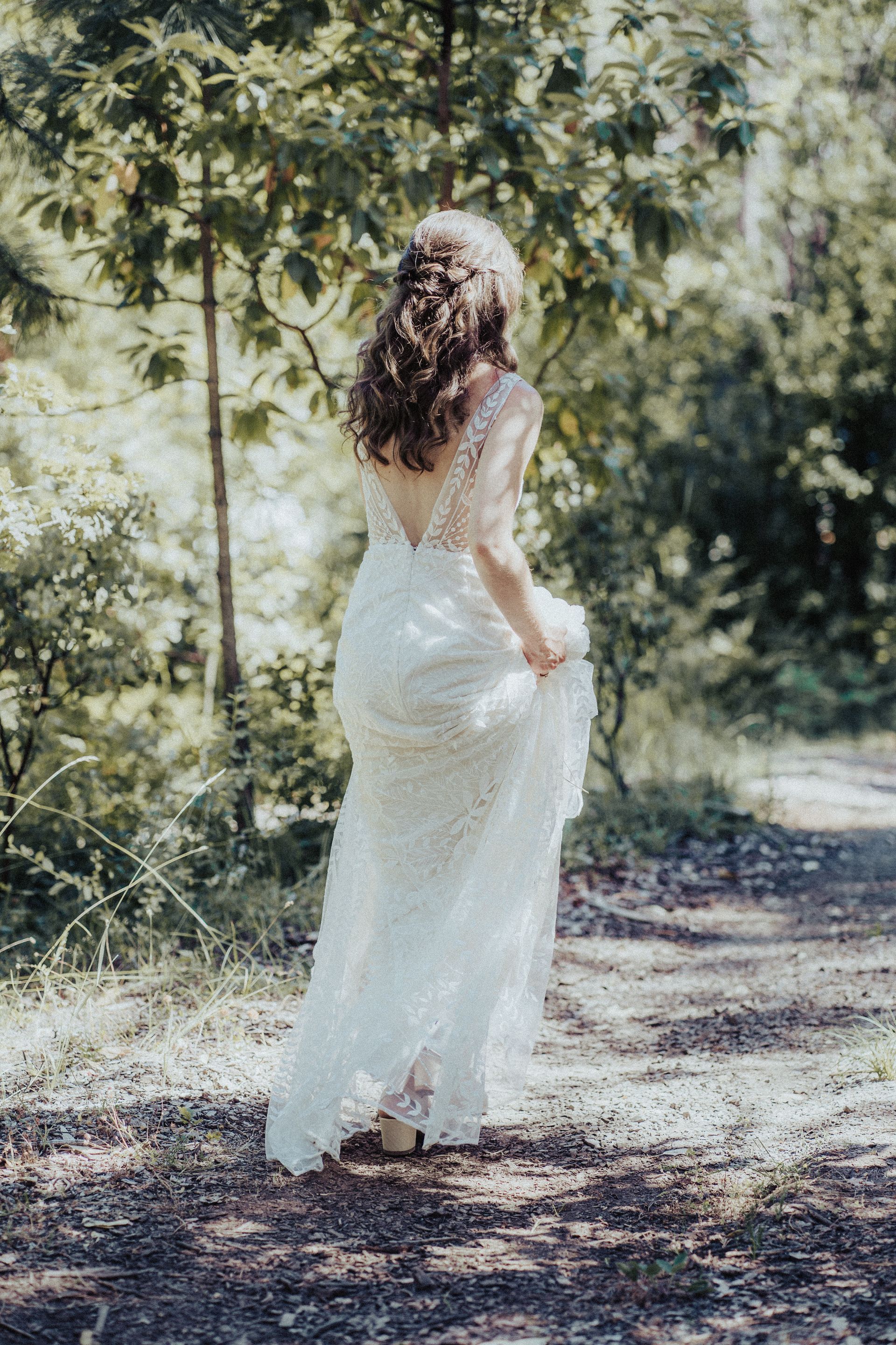 A woman in a wedding dress is walking down a path in the woods.