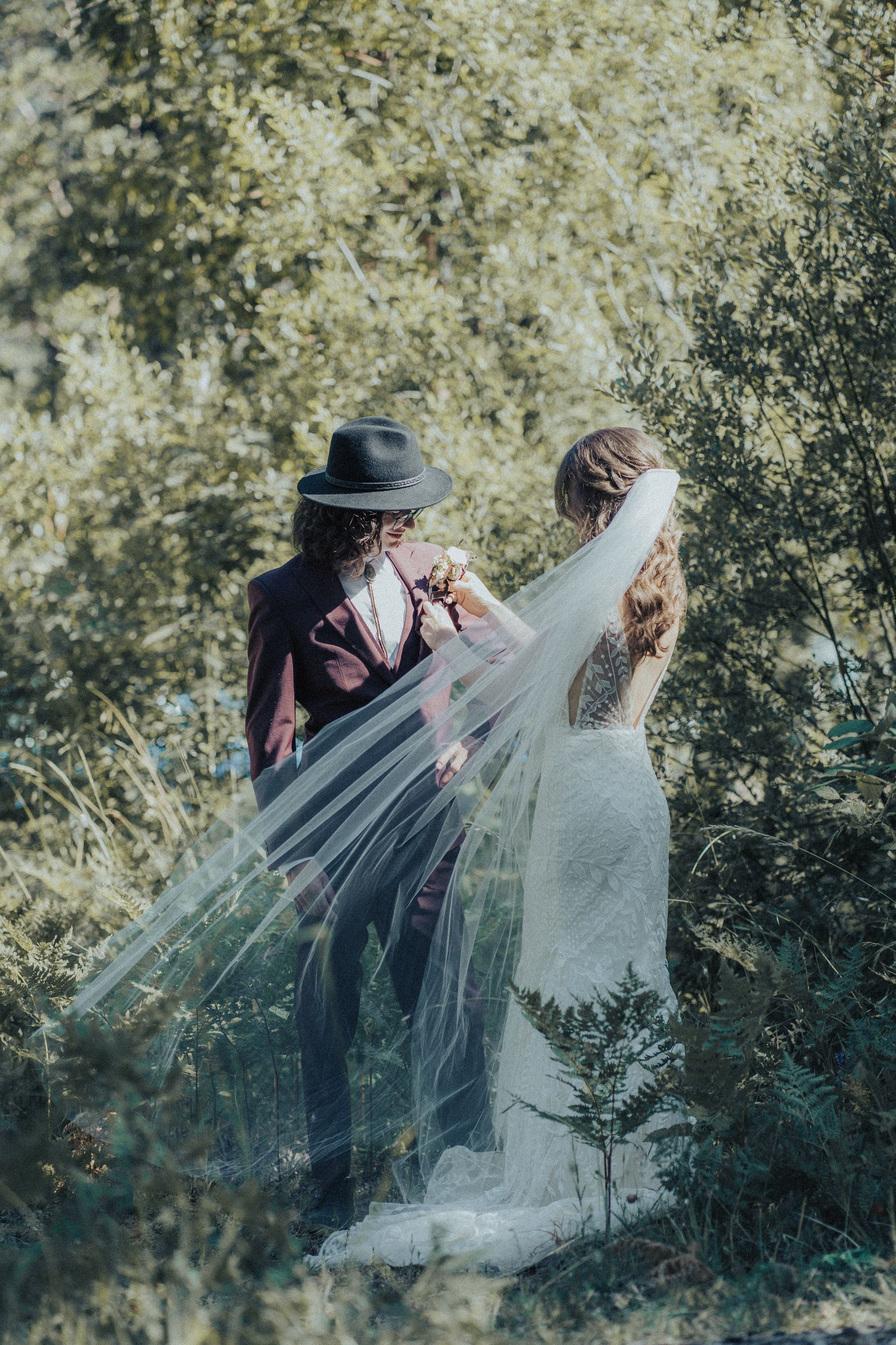 A bride and groom are standing in a field with a veil blowing in the wind.