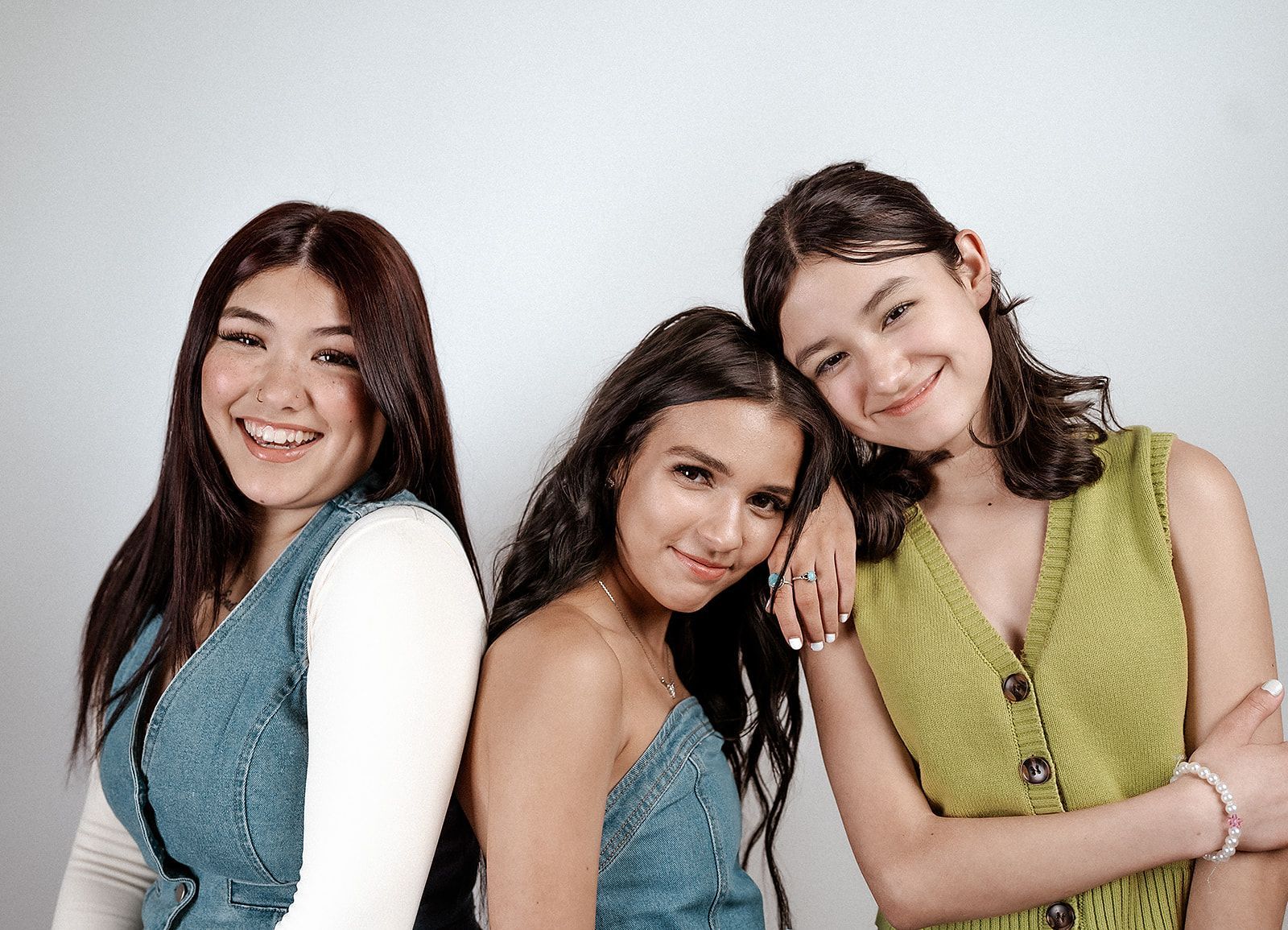 Three smiling young women posing together against a white backdrop.
