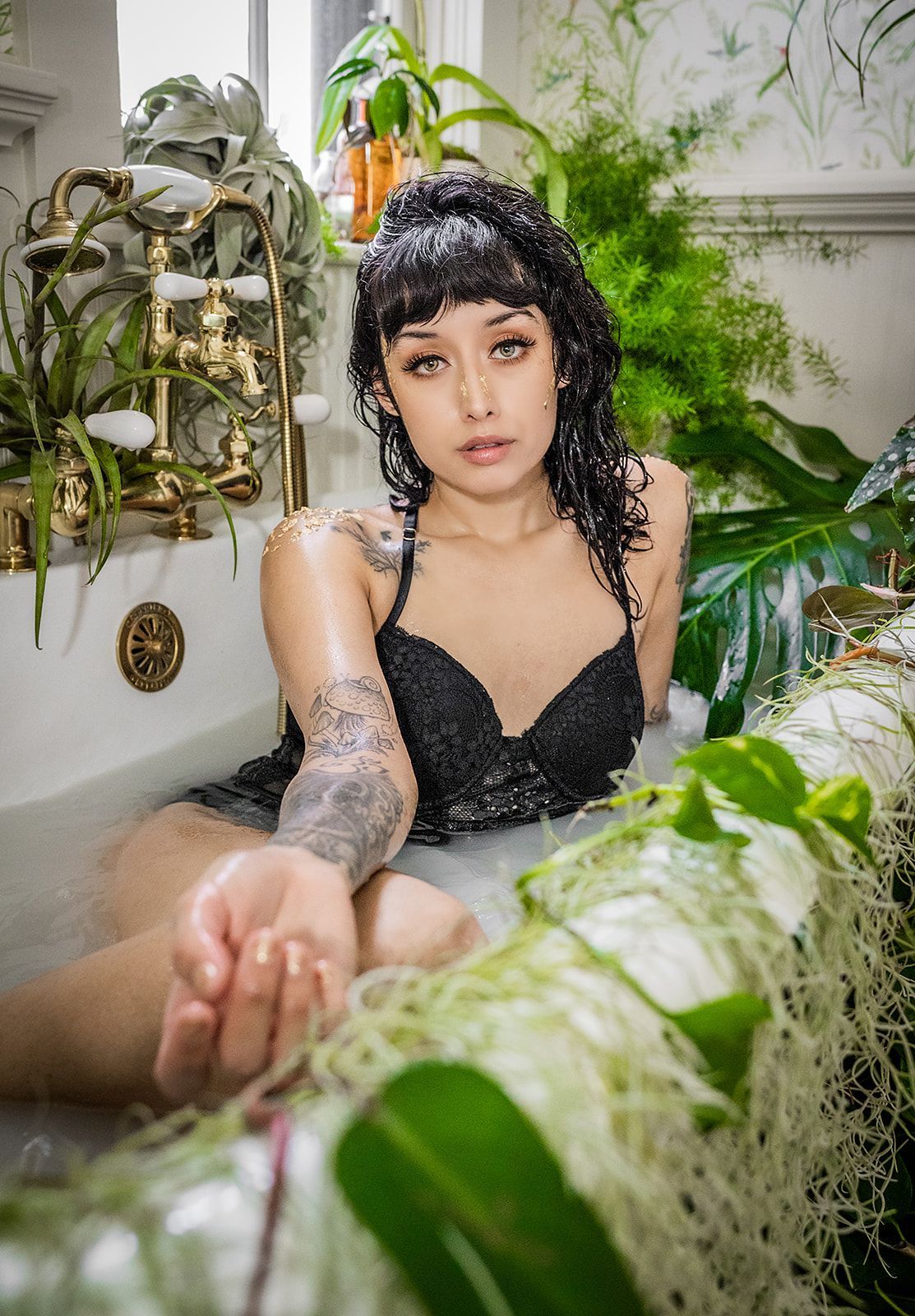 A woman is laying in a bathtub surrounded by plants.