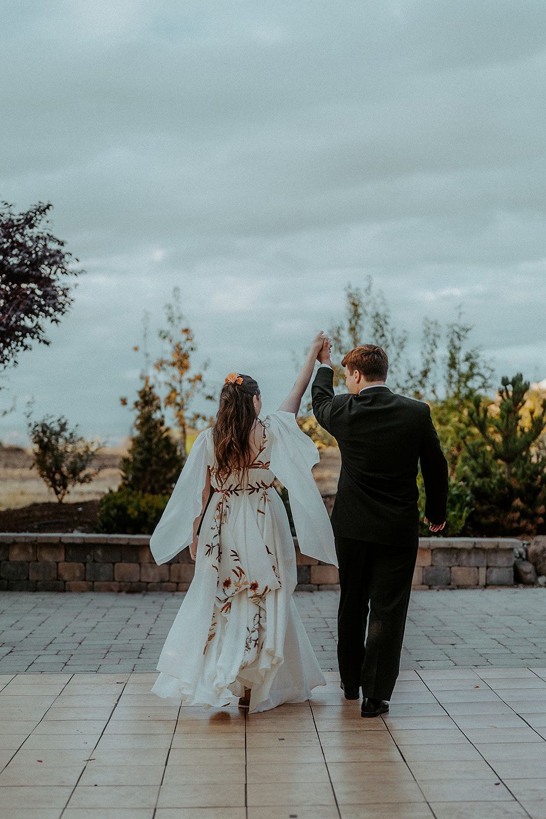 A bride and groom are walking down a sidewalk holding hands.