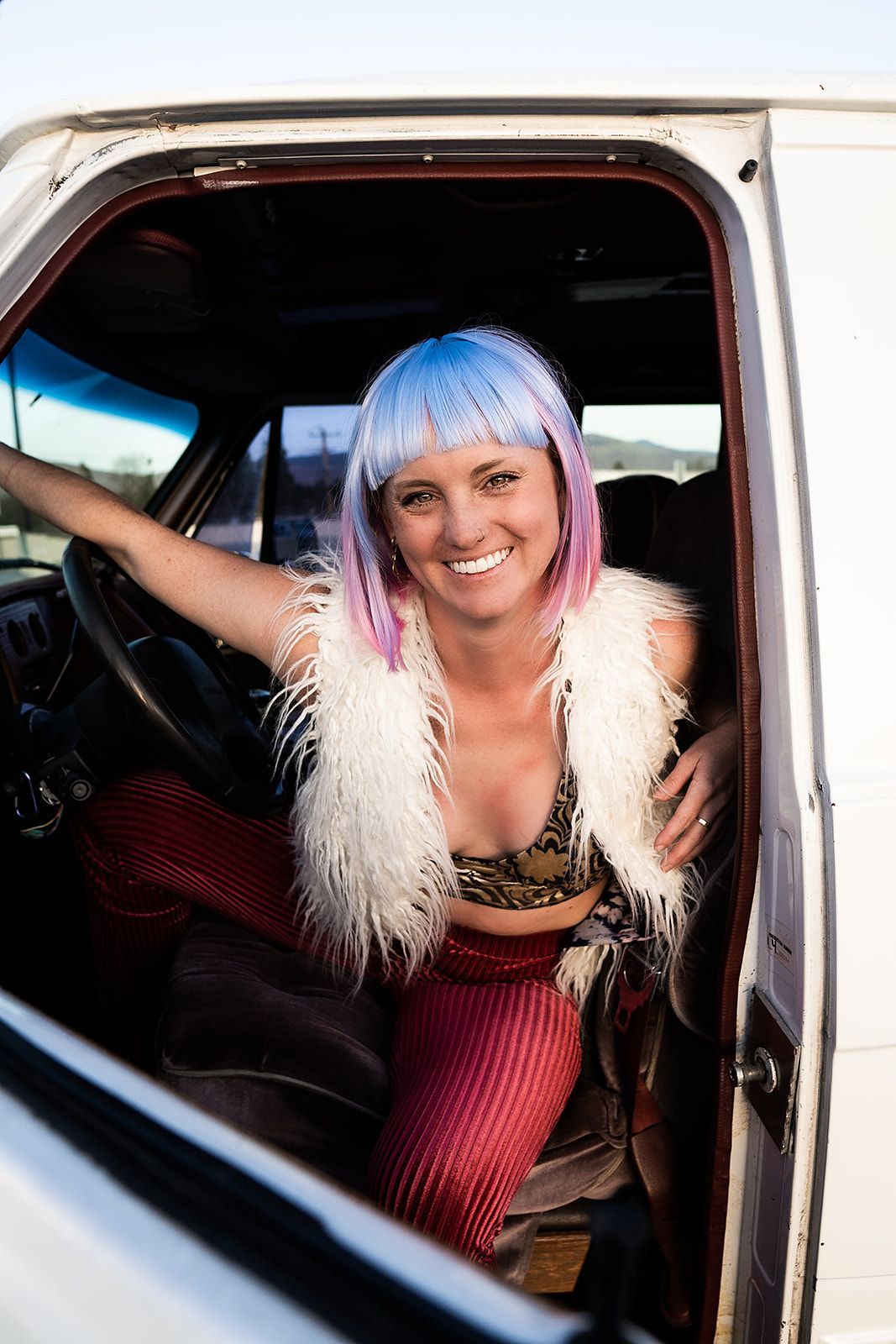 A woman with pink hair is sitting in the driver 's seat of a white van.