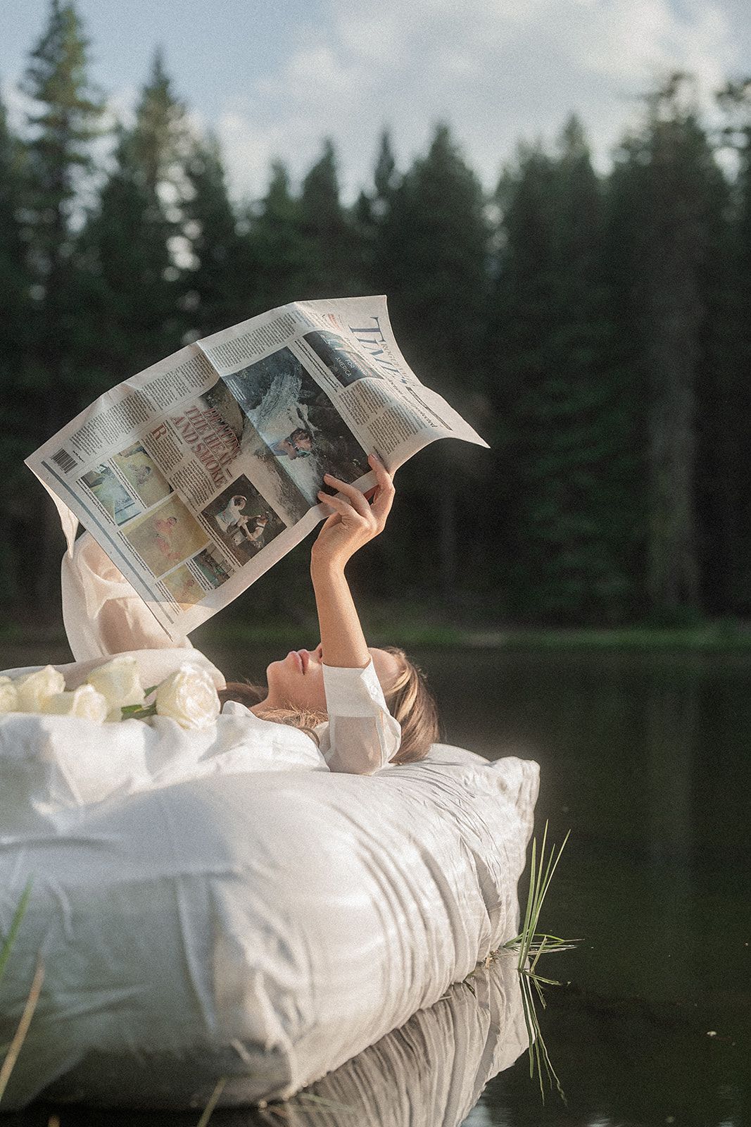 A woman is laying on a raft in the water reading a newspaper.