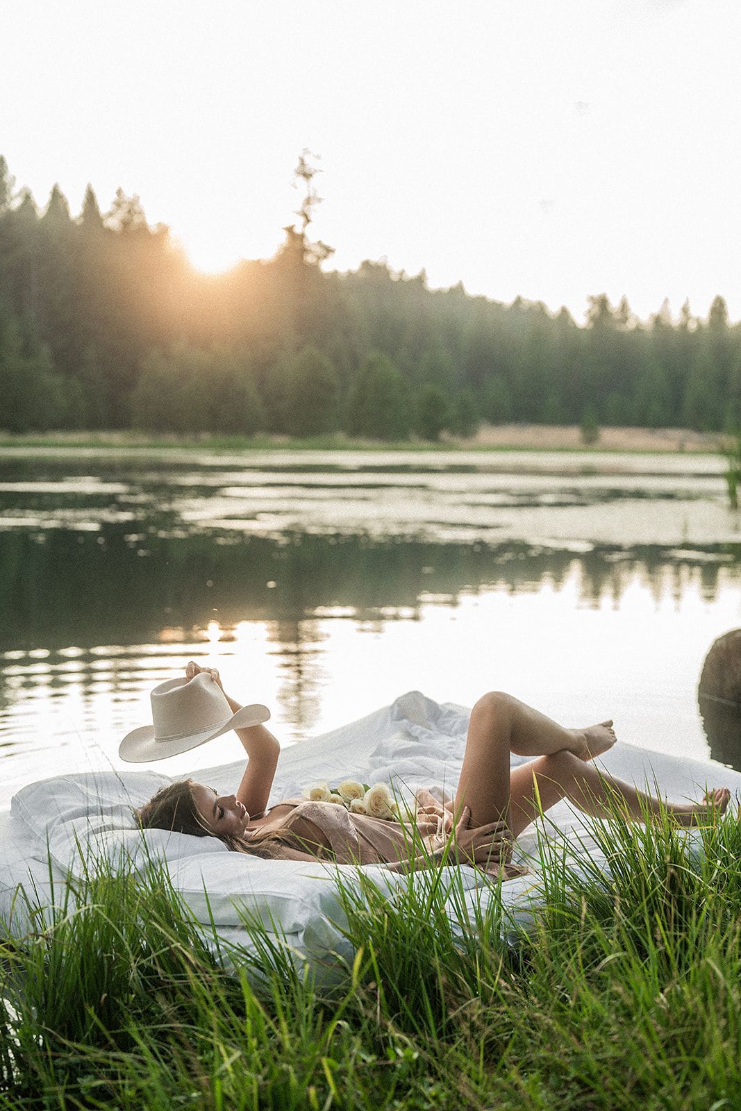 A woman is laying on a bed next to a lake.