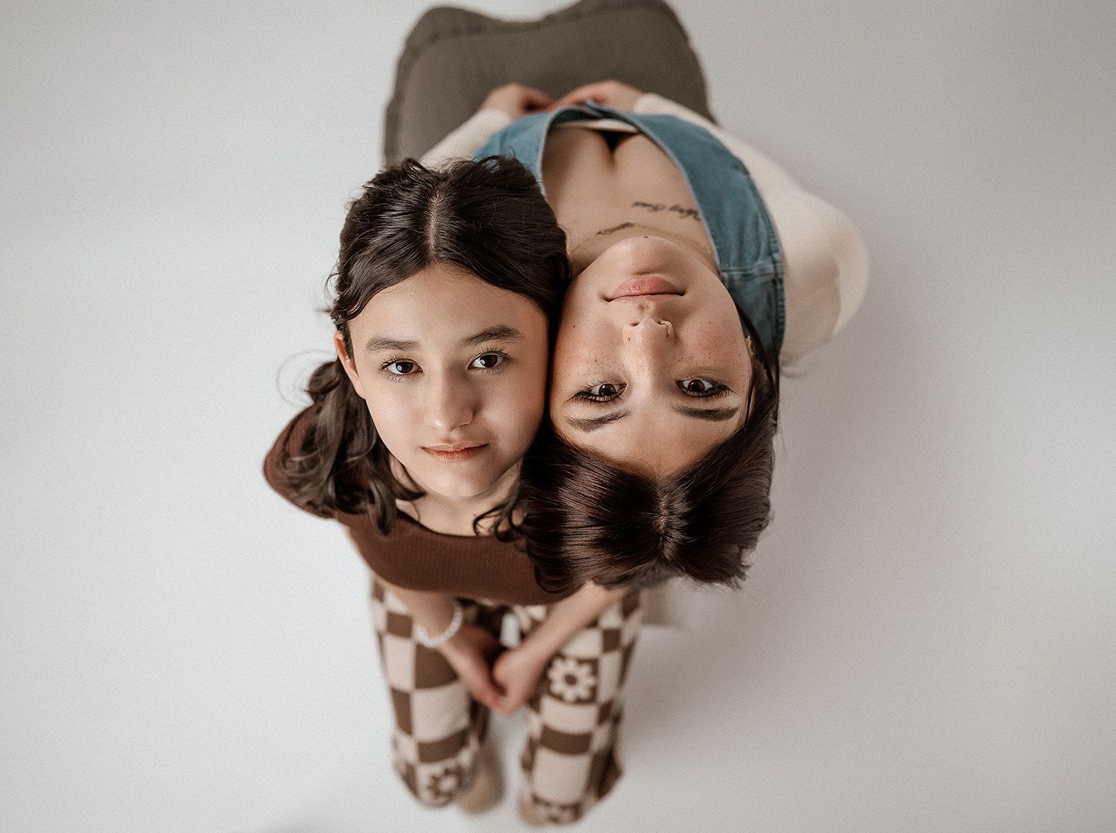 A mother and daughter are hugging each other and looking up at the camera.