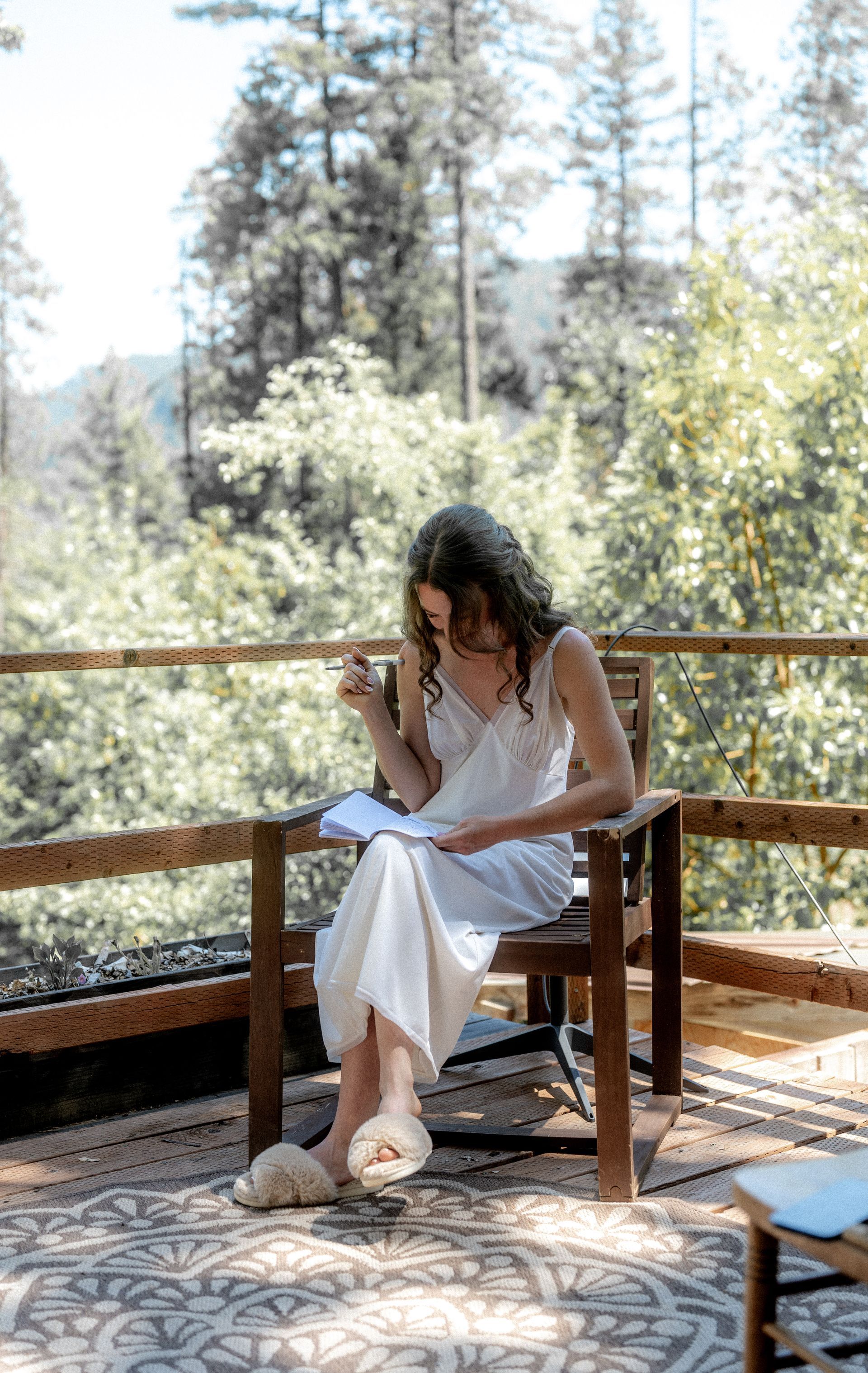 A woman is sitting in a chair on a deck reading a book.