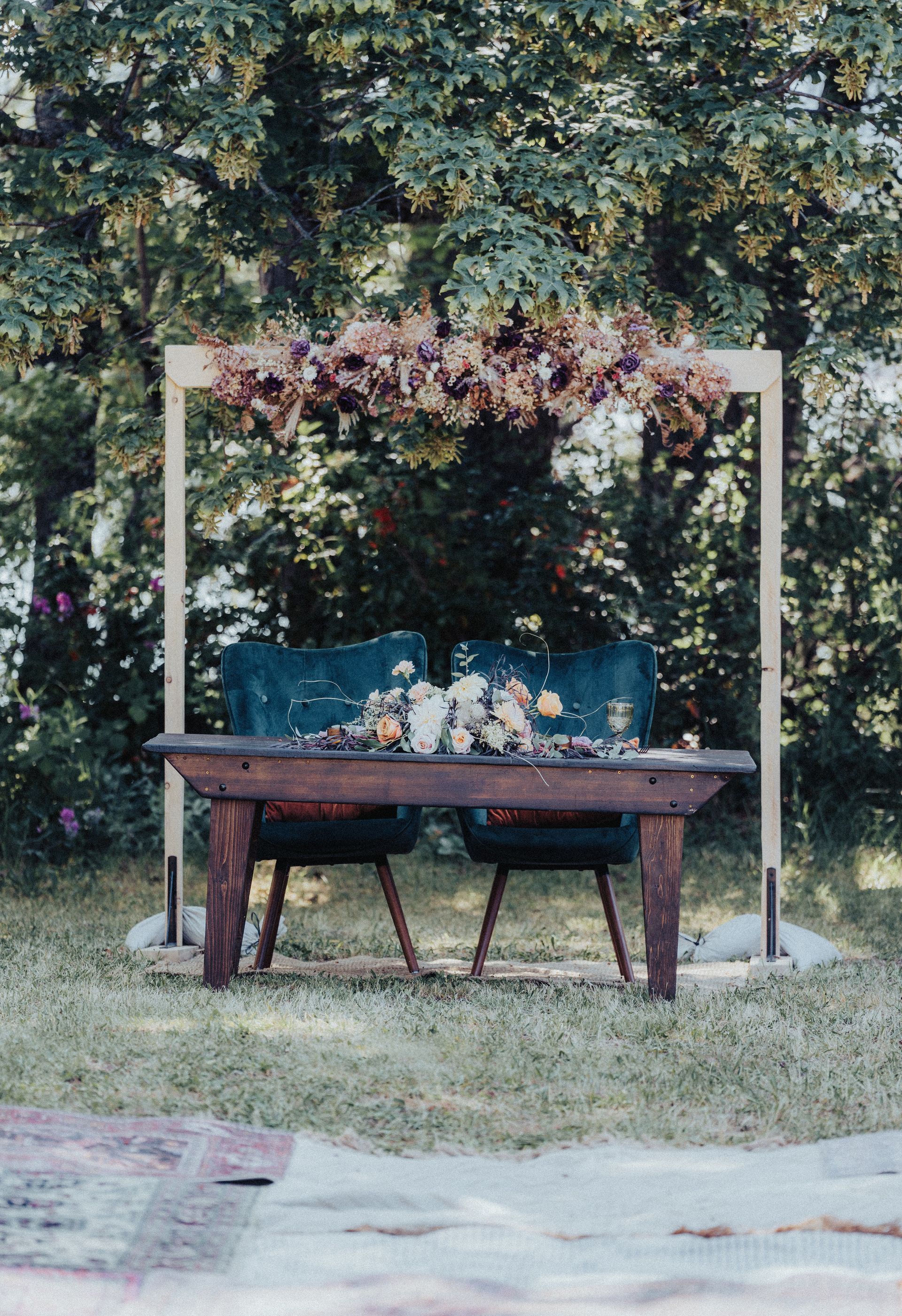A wooden table and chairs are sitting in the grass under a wooden arch.