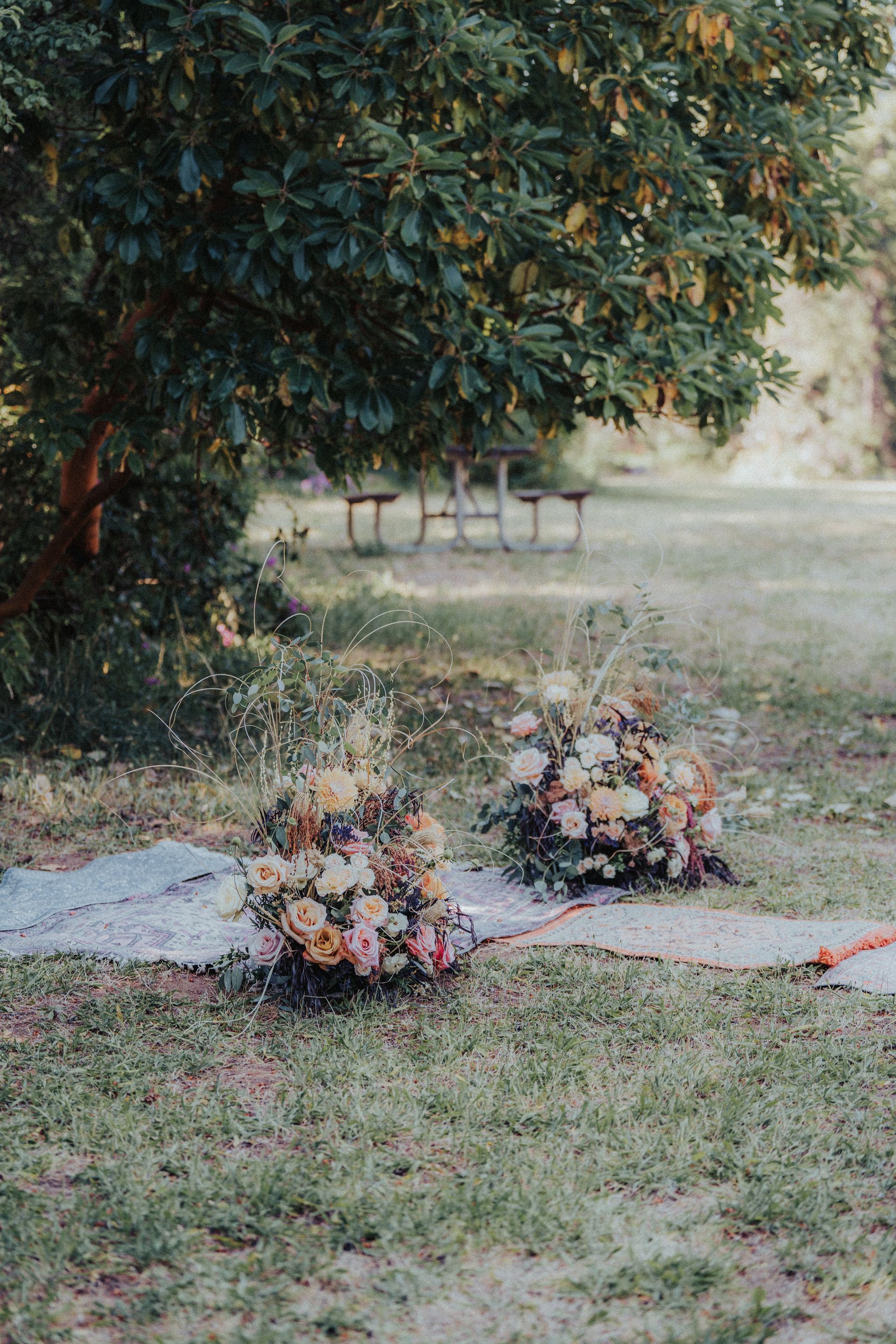 Two bouquets of flowers are sitting on a blanket in the grass under a tree.