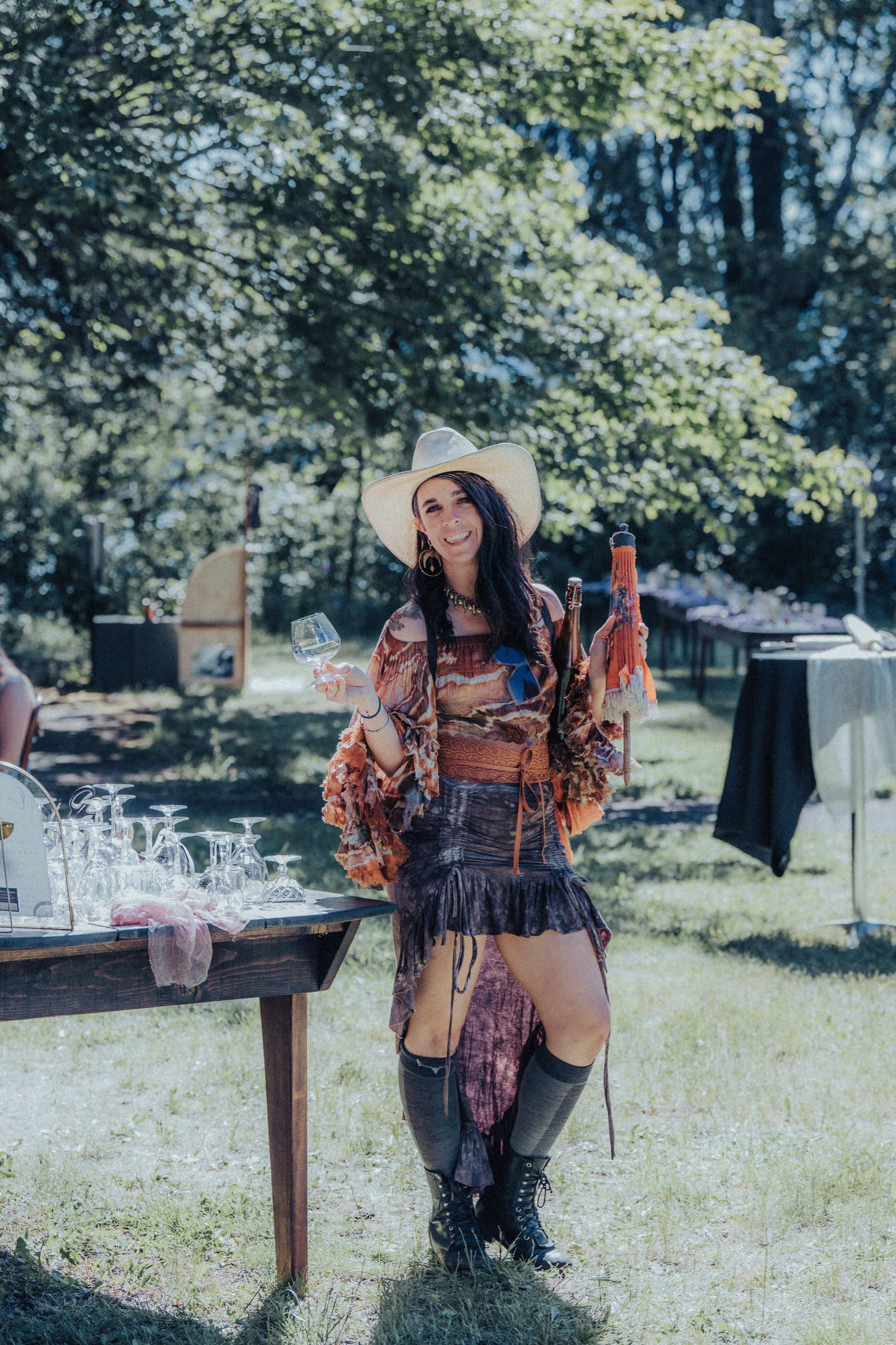 A woman in a cowboy hat is standing in front of a table holding a bottle of wine.