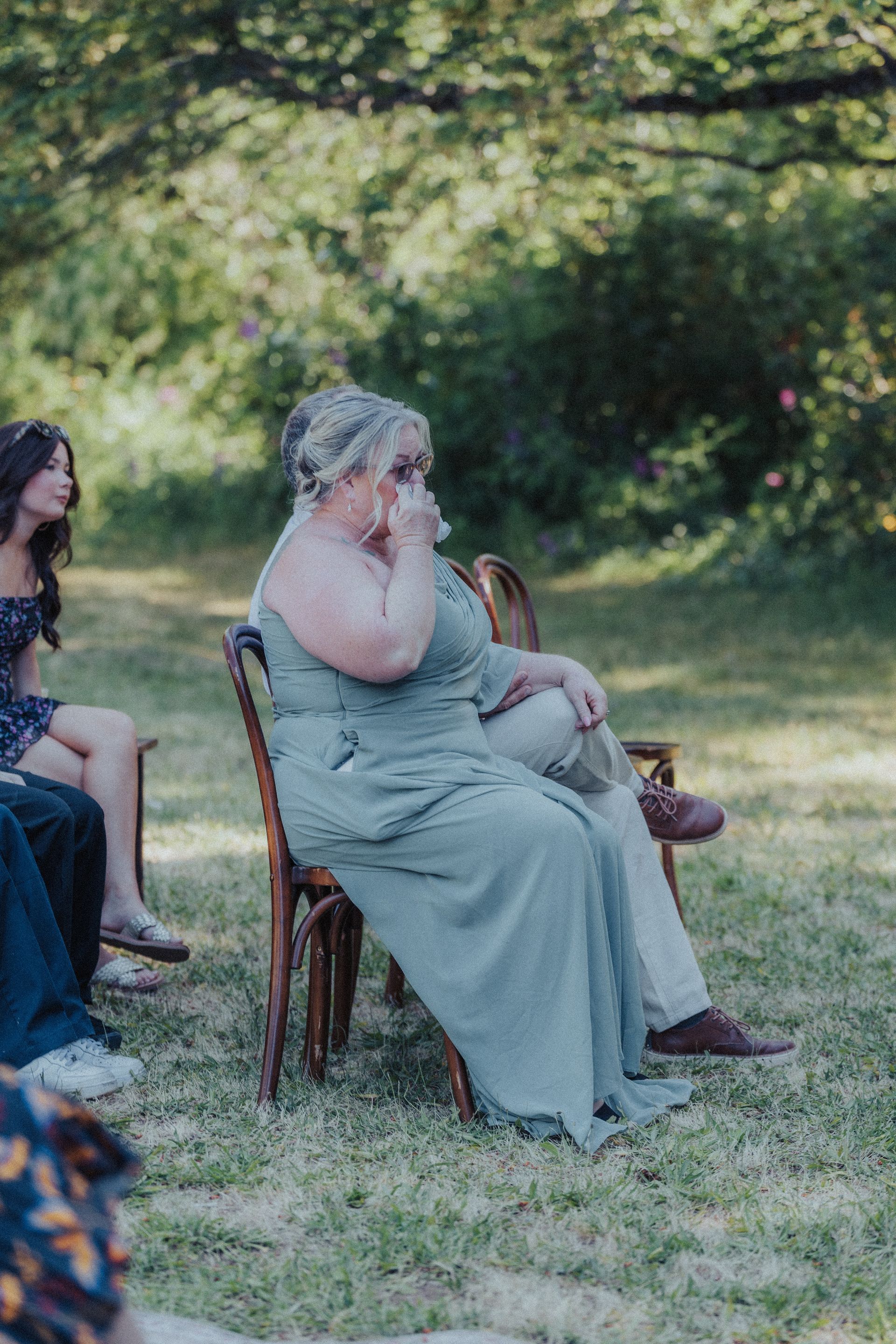 A woman in a green dress is sitting in a chair in the grass.