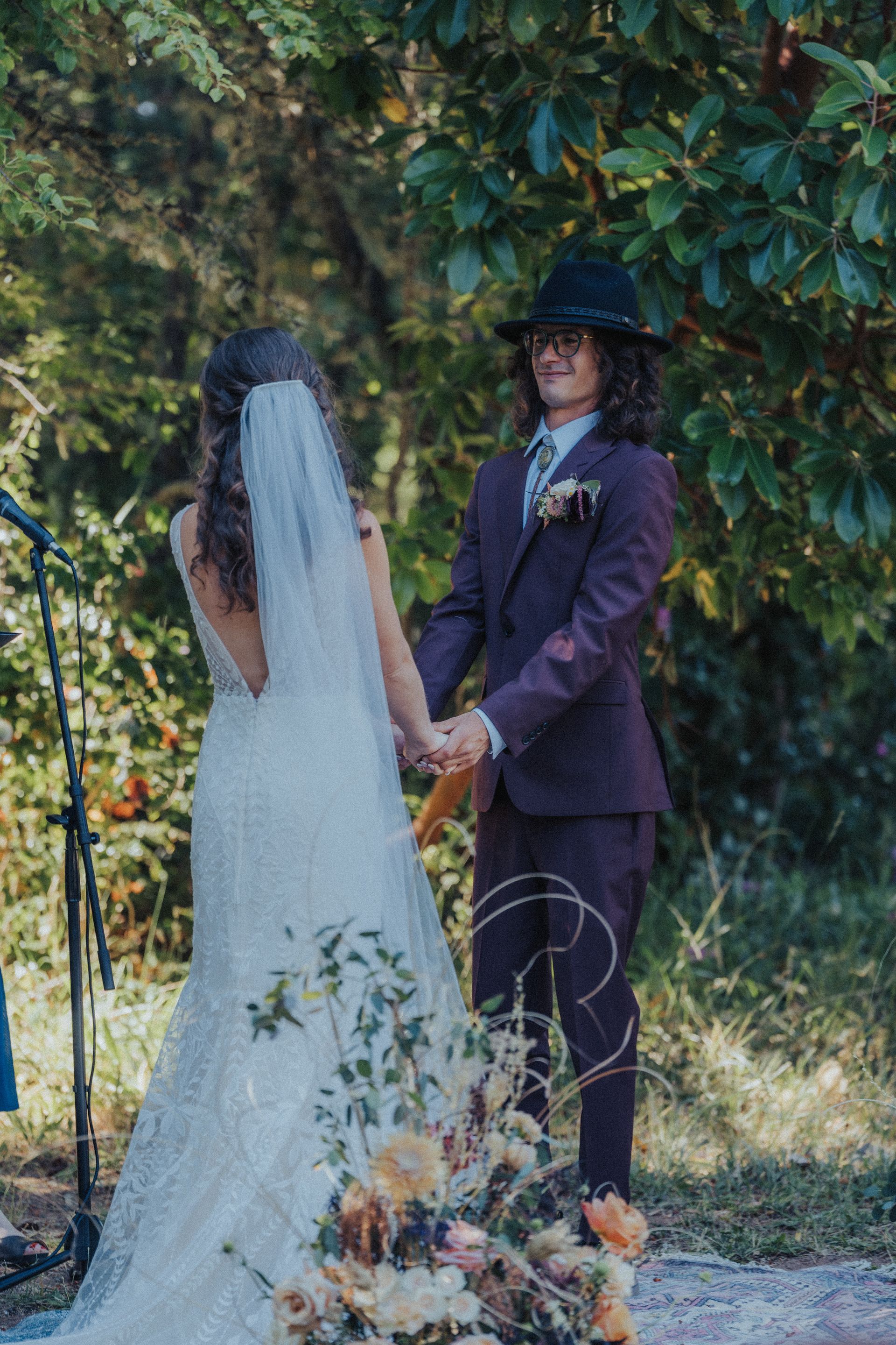 A bride and groom are holding hands during their wedding ceremony in the woods.