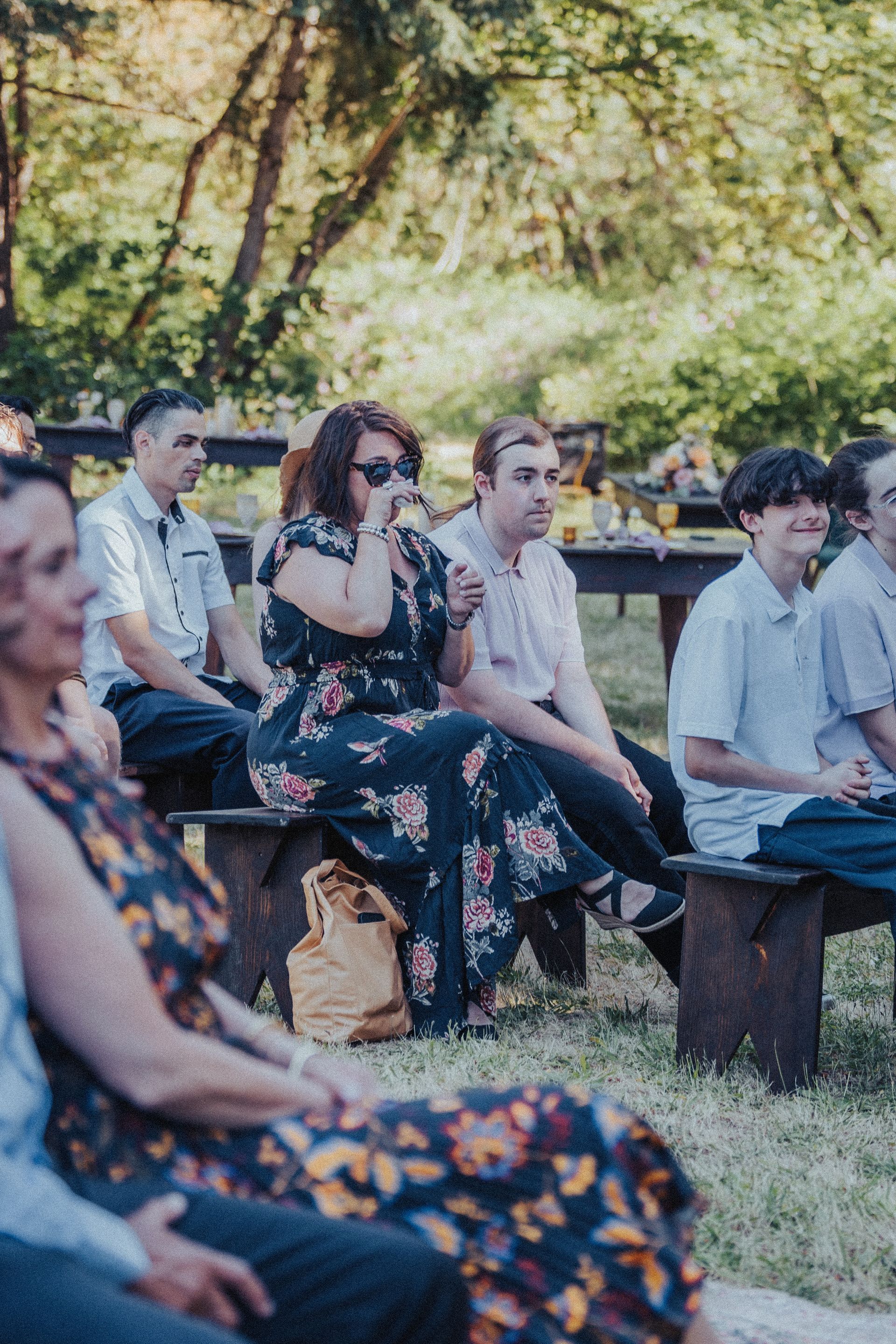 A group of people are sitting on wooden benches in the grass.