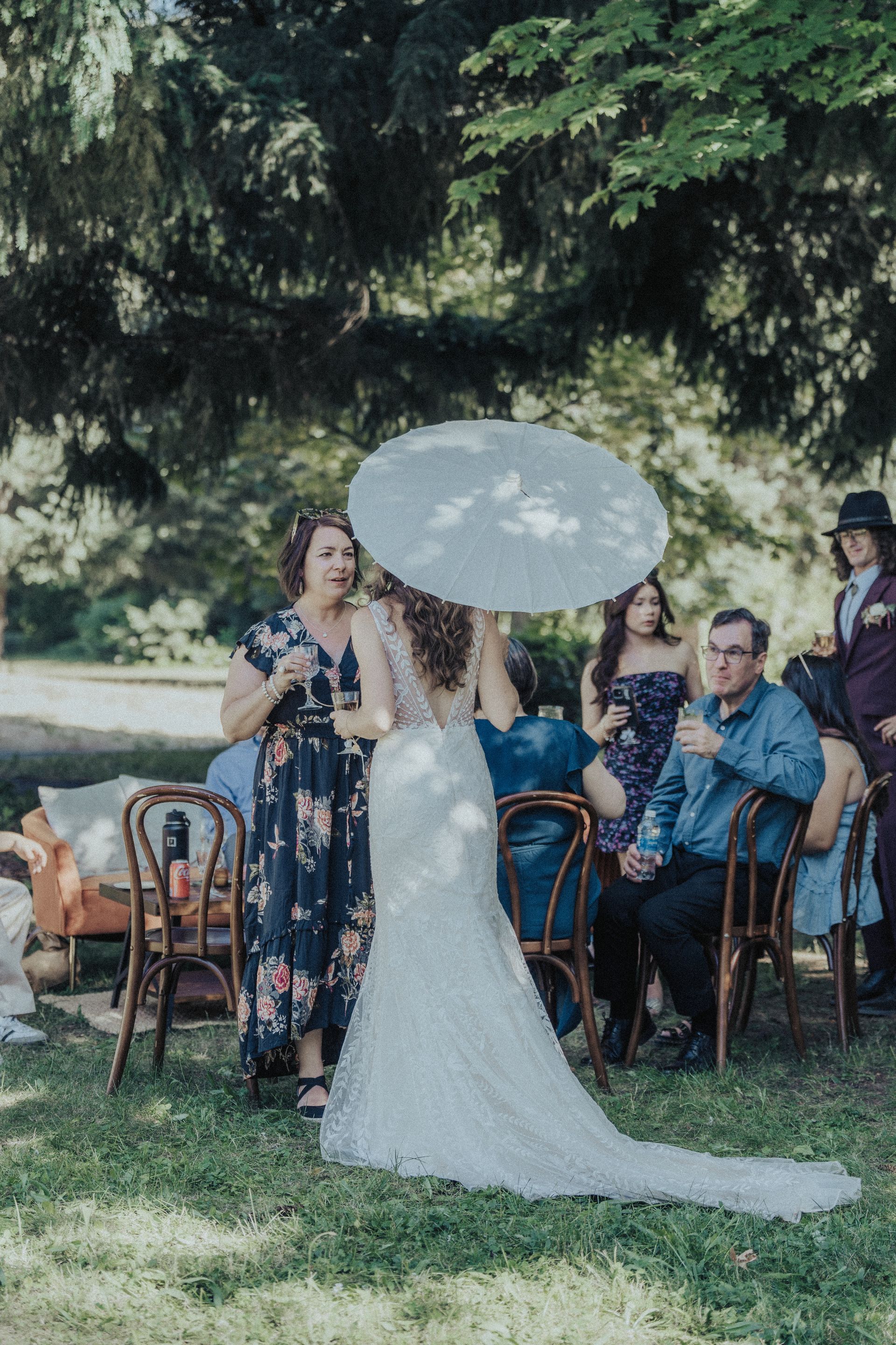 A bride in a wedding dress is holding an umbrella in front of a group of people.