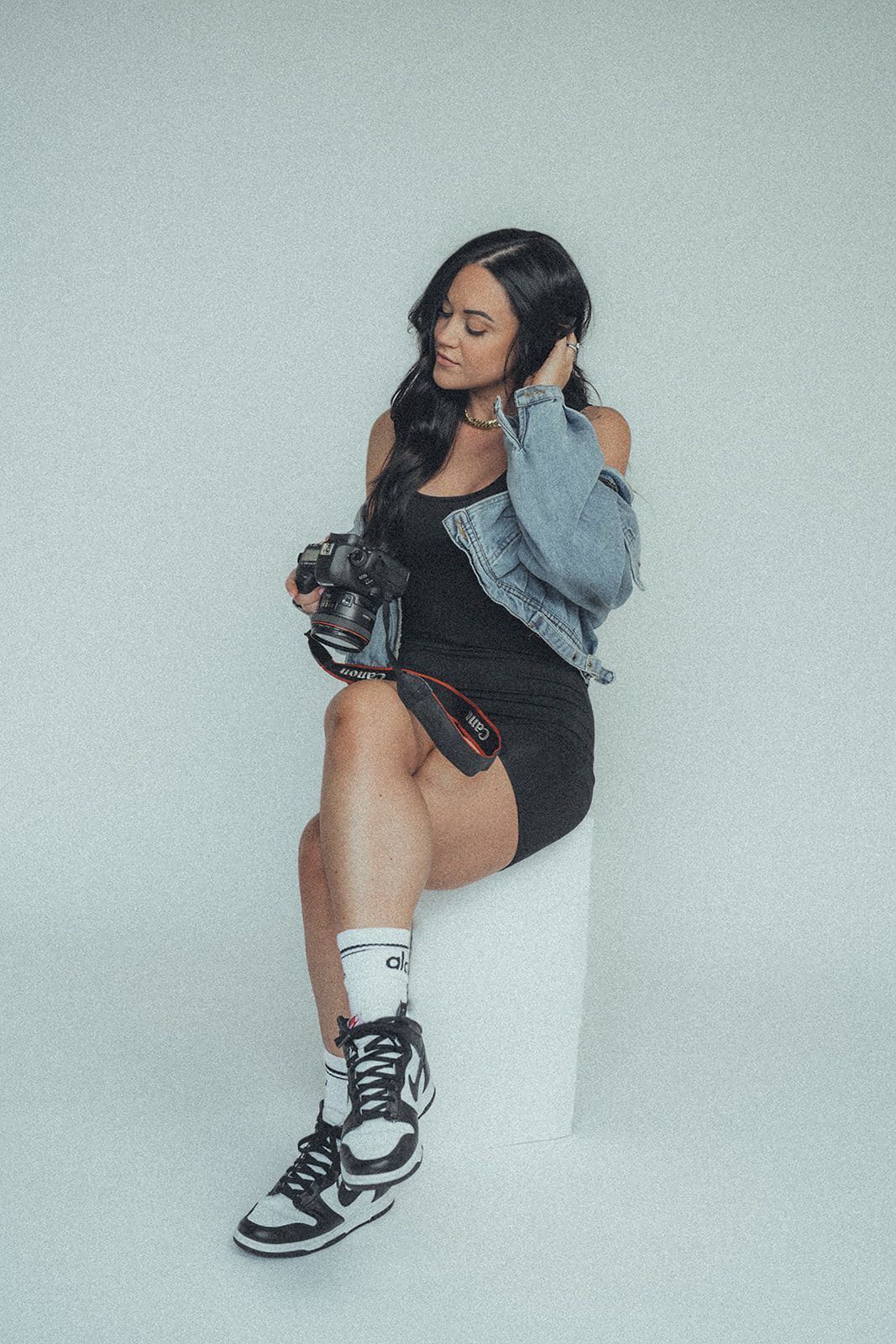 A woman is sitting on a stool holding a camera.