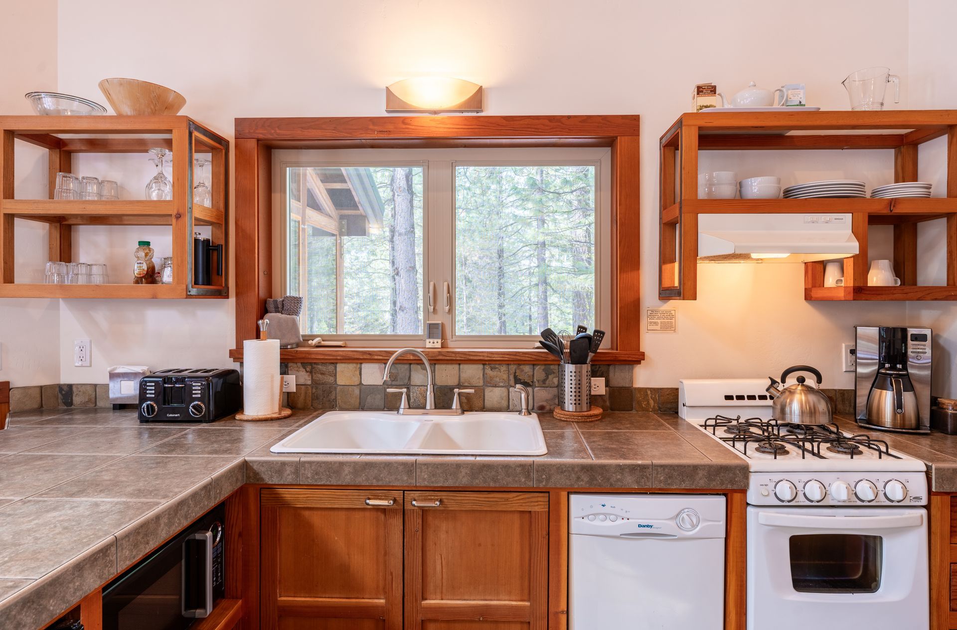A kitchen with a sink , stove , dishwasher , and window.