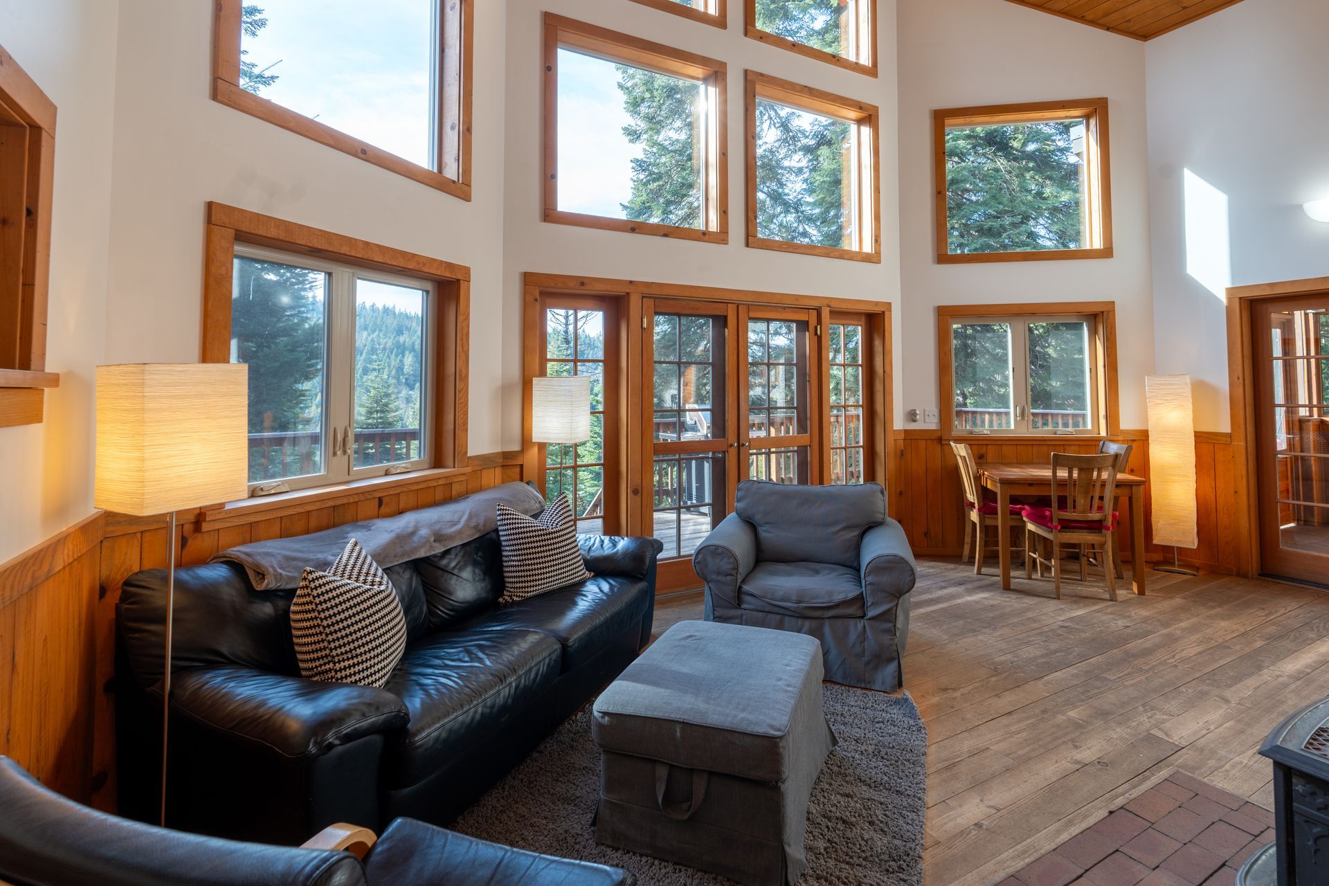 A living room with a couch , chair , ottoman and lots of windows.