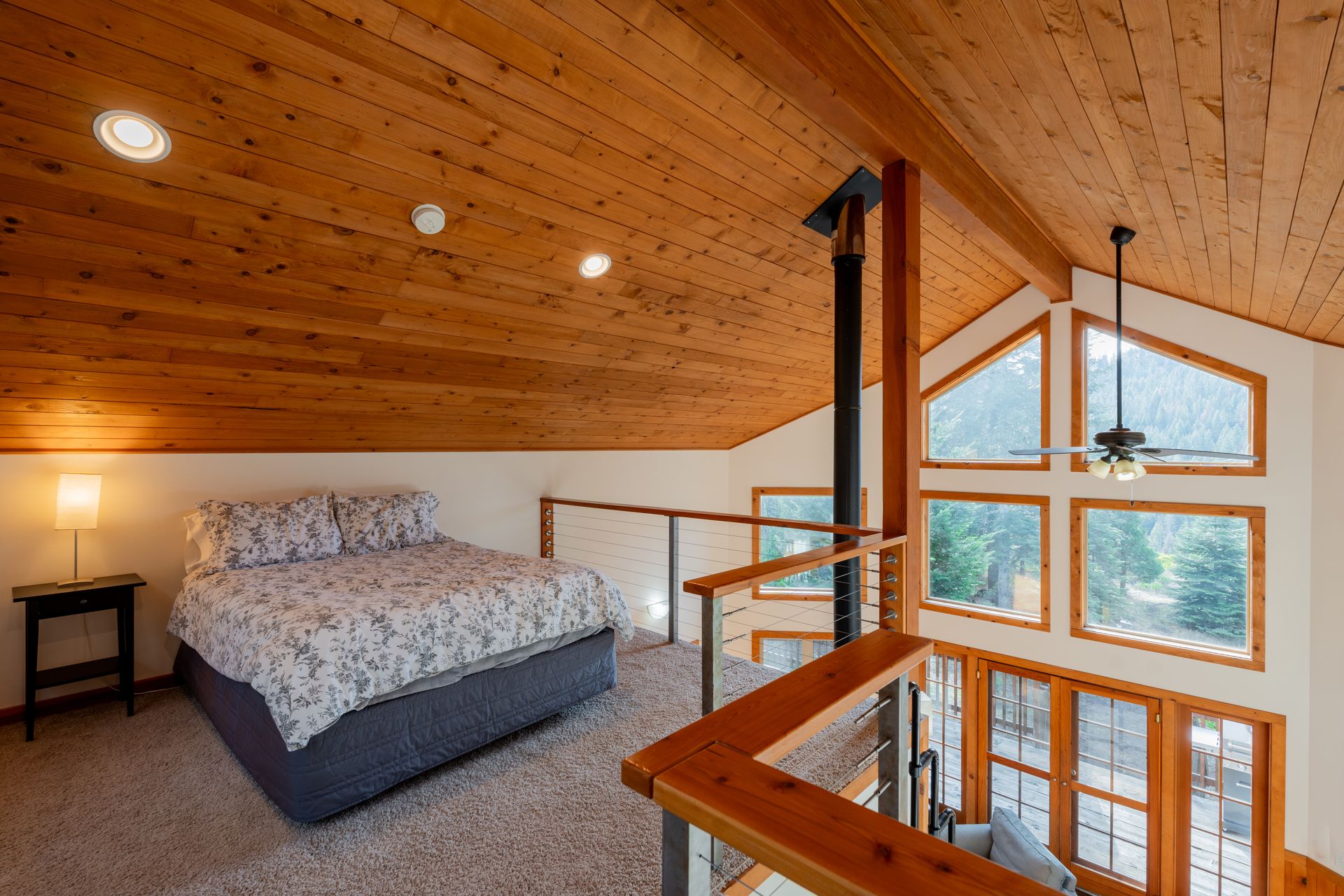 A bedroom with a bed , ceiling fan , and lots of windows.