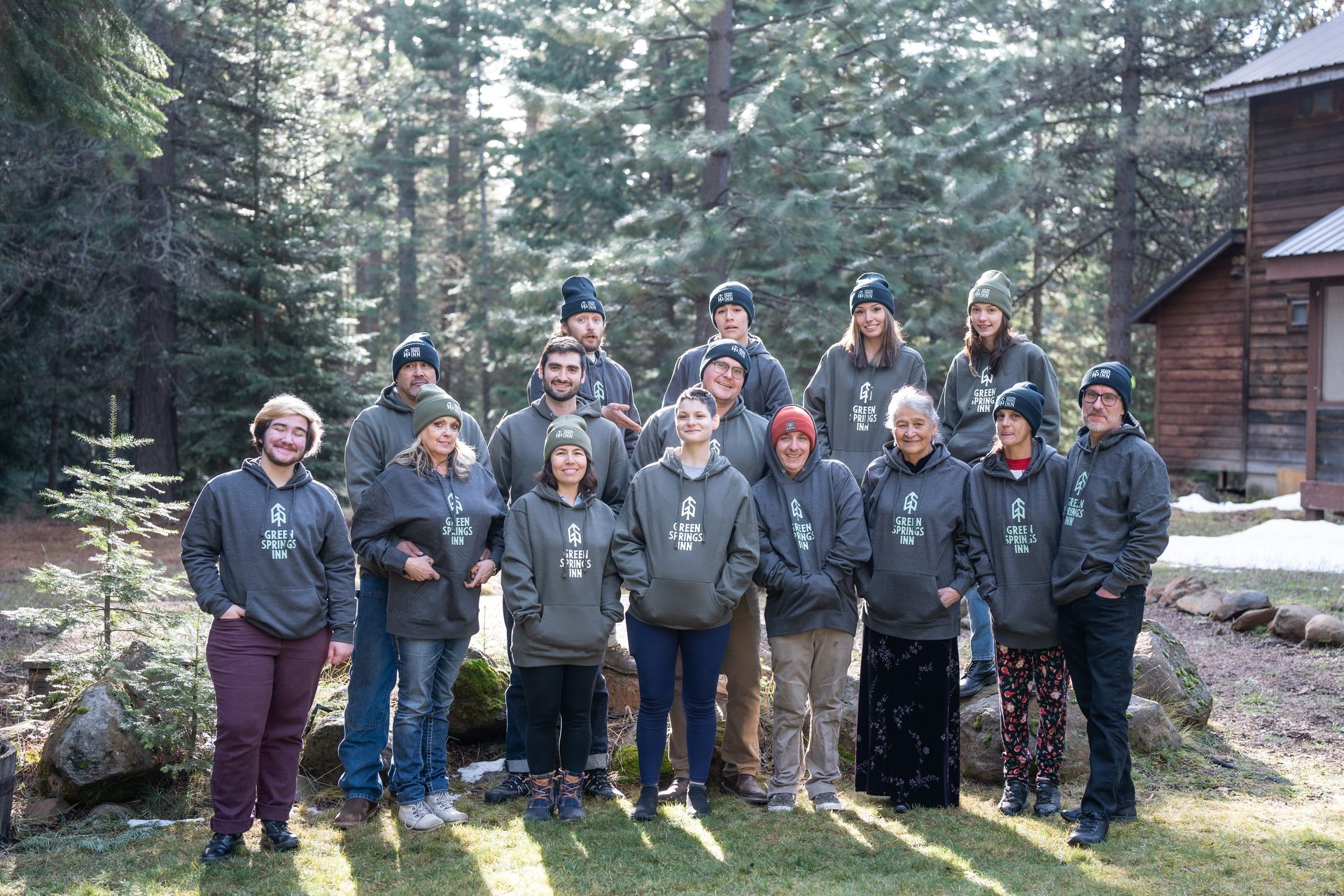 A group of people are posing for a picture in front of a cabin in the woods.