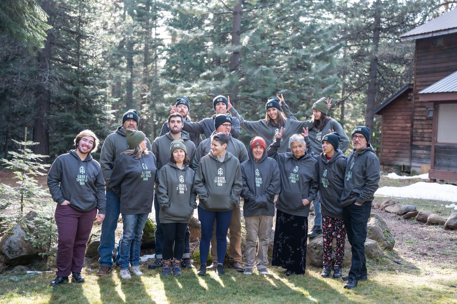 A group of people are posing for a picture in front of a cabin in the woods.