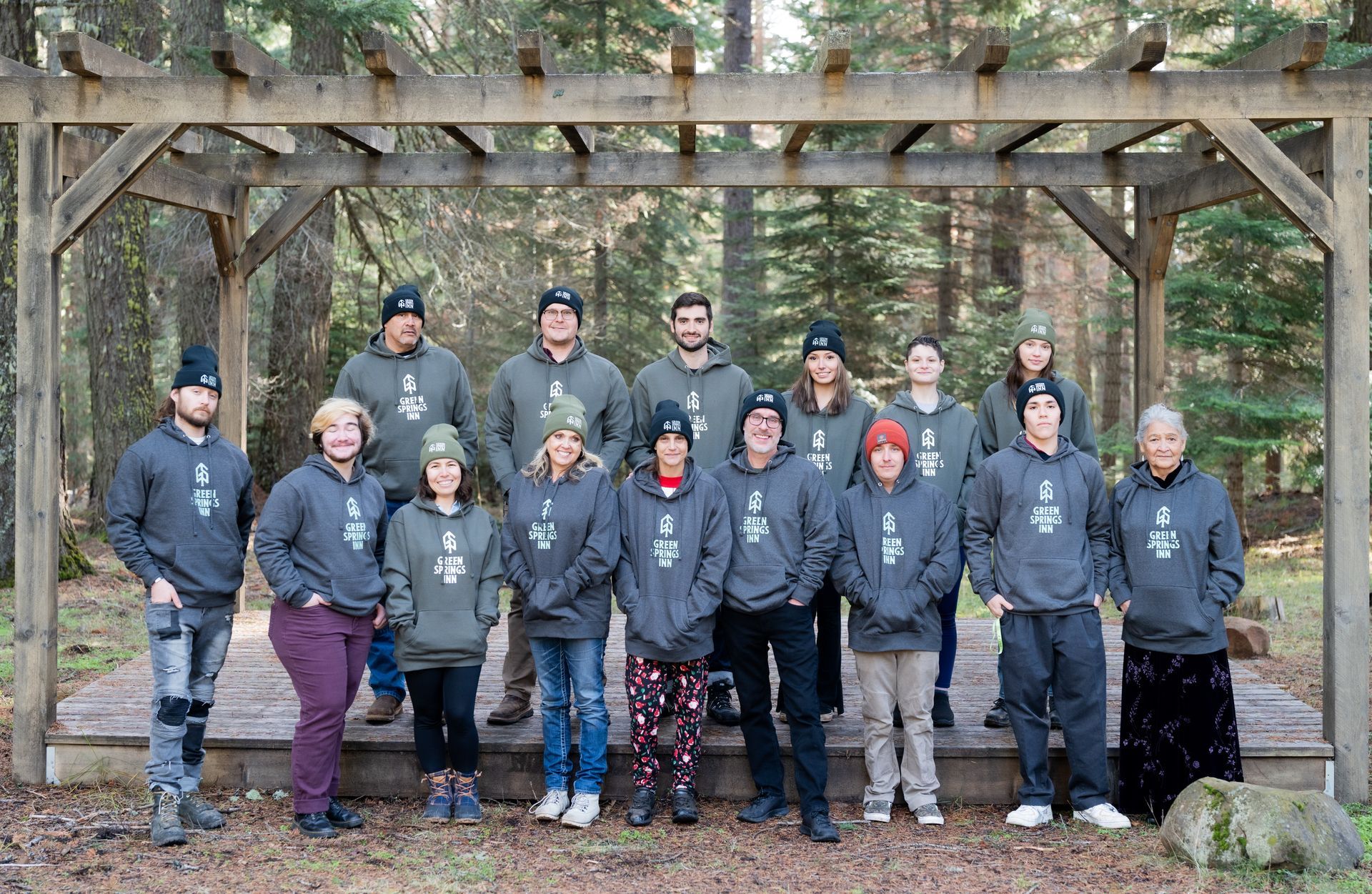 A group of people are posing for a picture under a pergola in the woods.