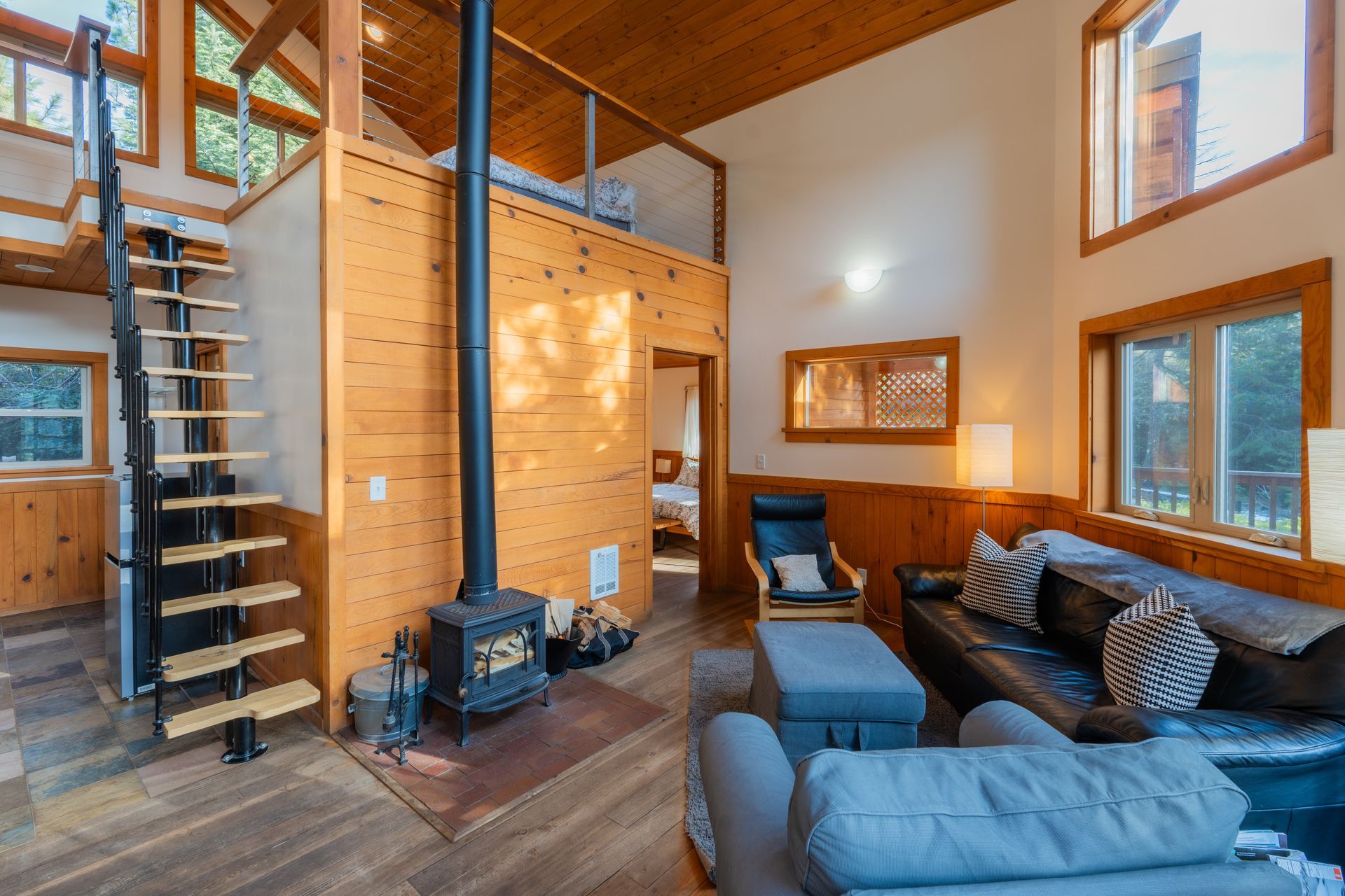 A living room in a cabin with a wood stove and stairs leading to the second floor.
