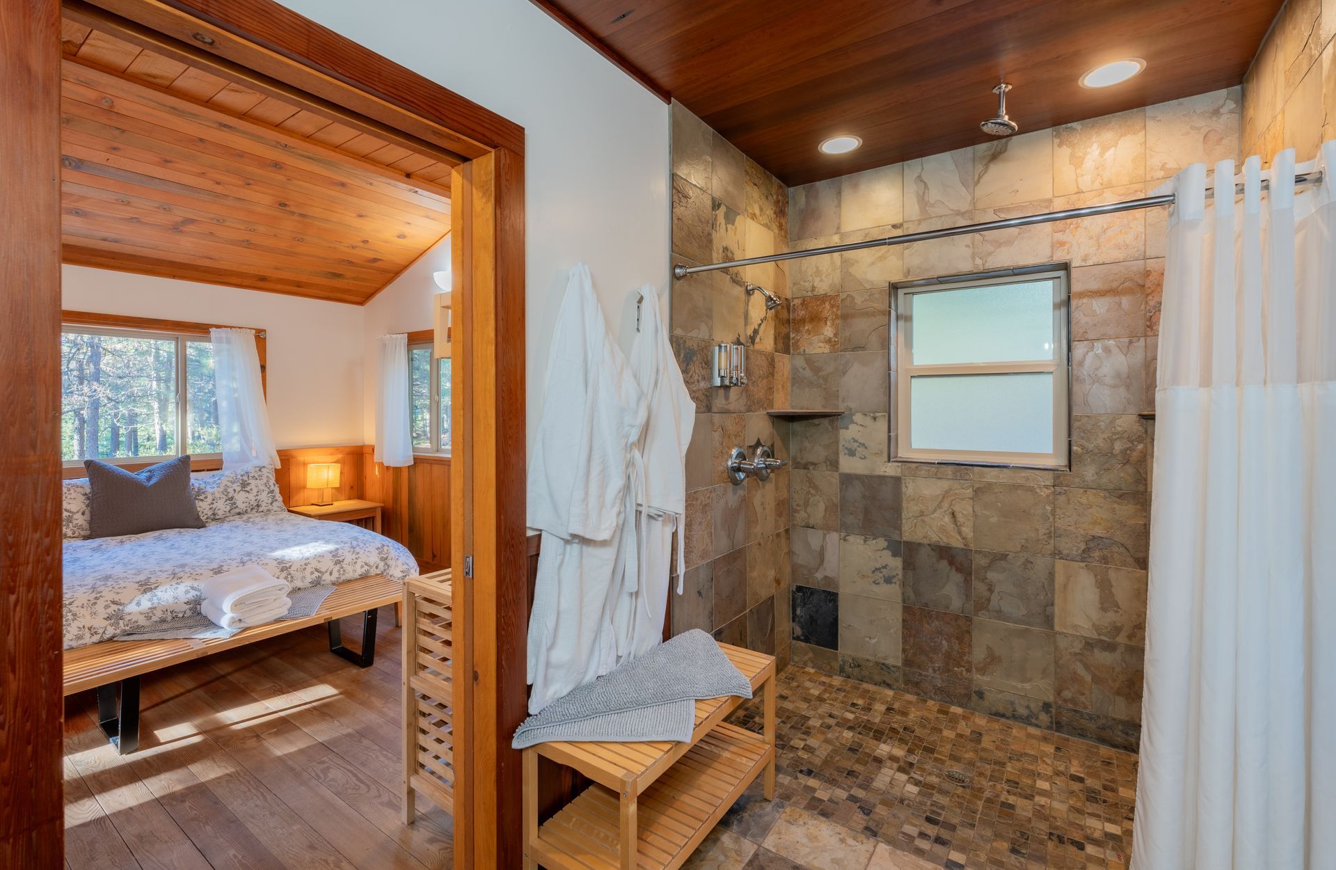 A bathroom with a walk in shower and a bed in the background.