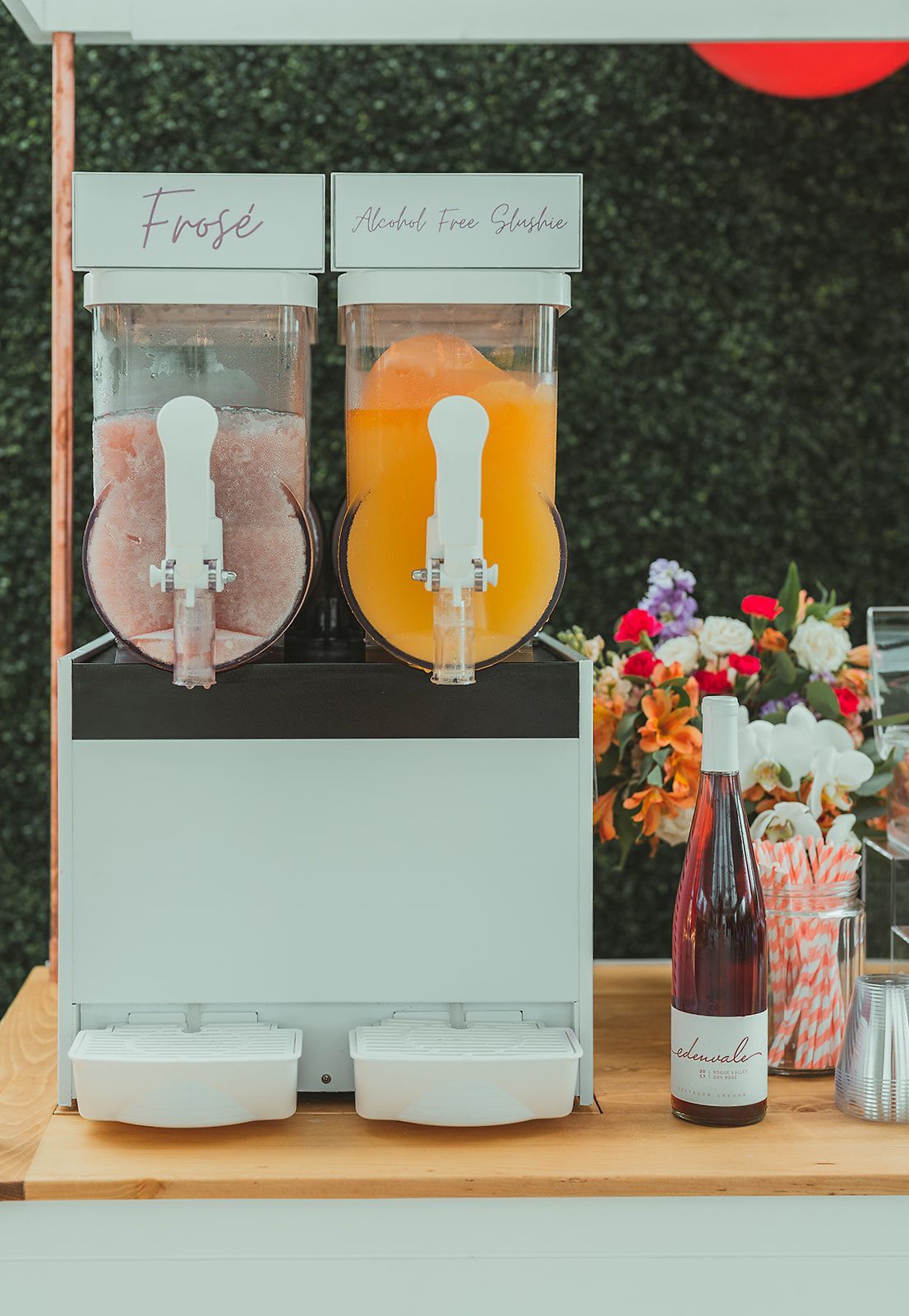 A drink dispenser is sitting on a wooden table next to a bottle of wine.