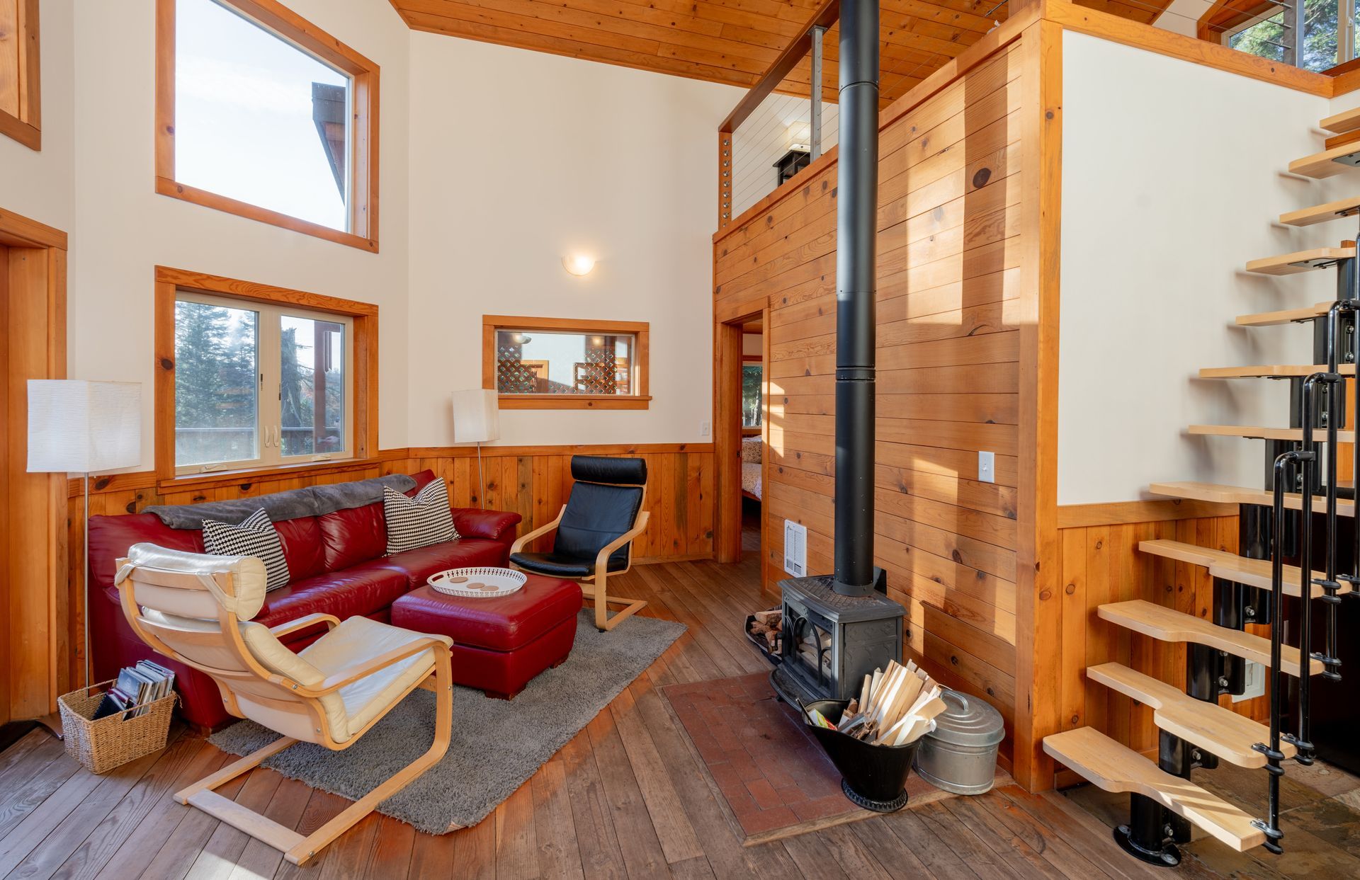 A living room with a red couch , chairs , stairs and a wood stove.